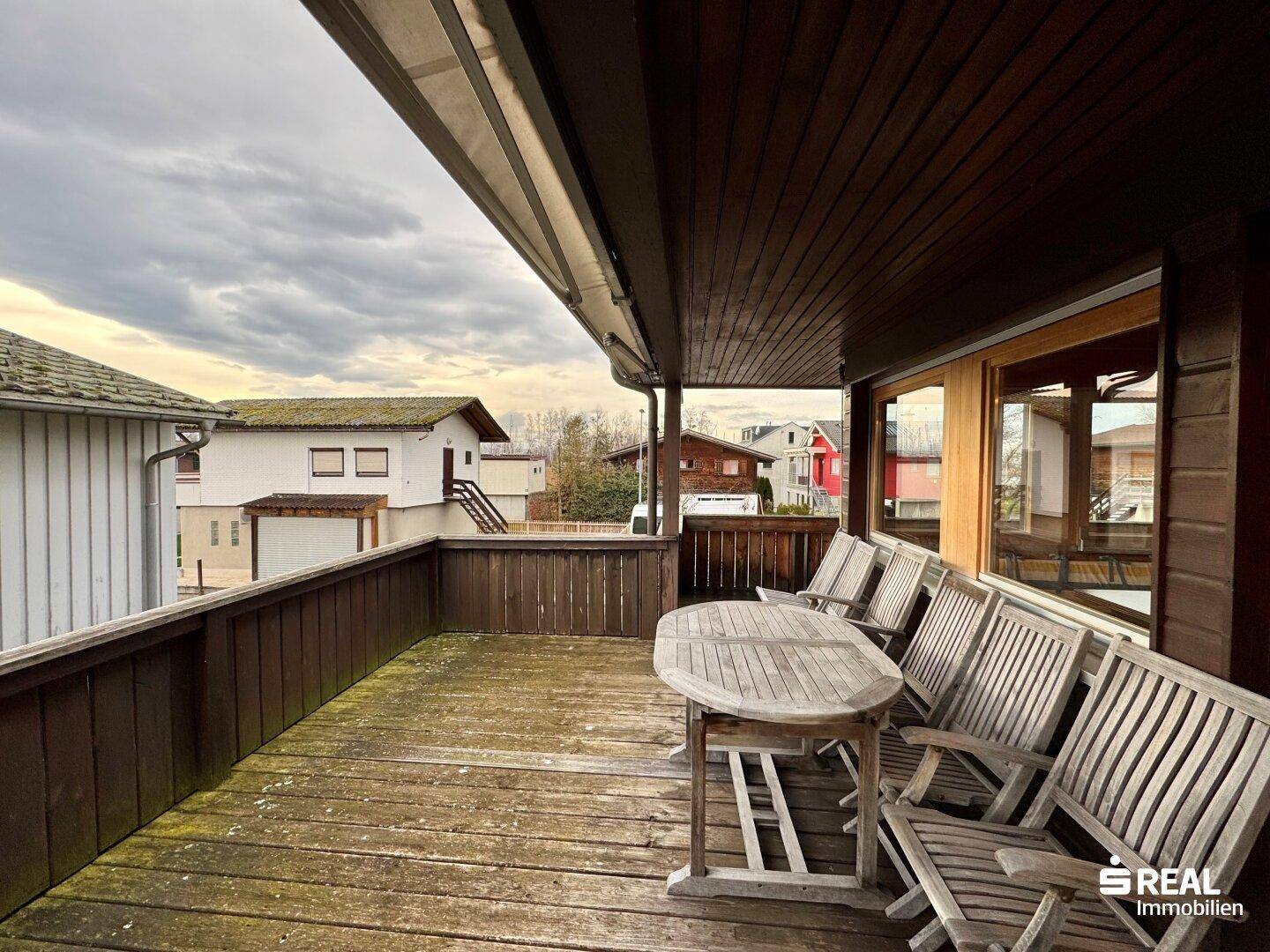 Große Holzterrasse mit Gartenmöbeln und Blick auf die Nachbarschaft.