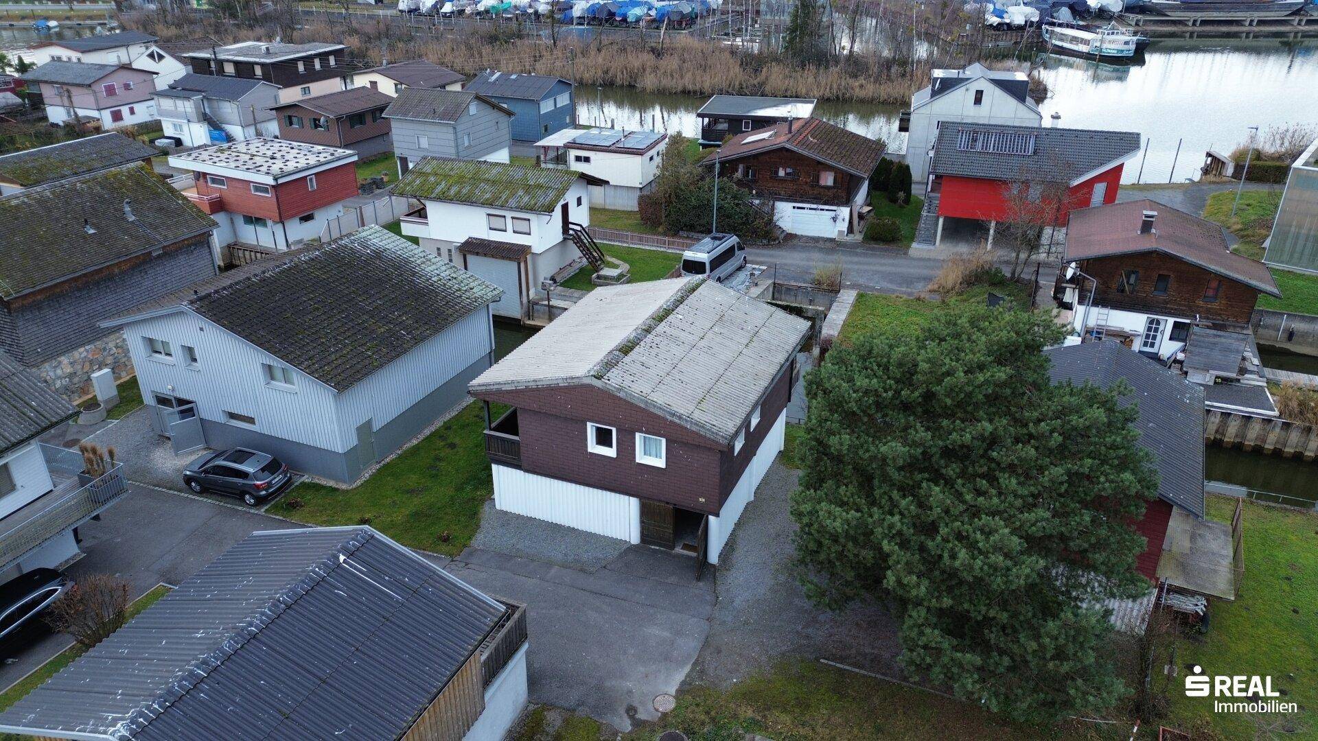 Luftaufnahme der Siedlung am See mit vielen Häusern und Bootsanlegestellen.