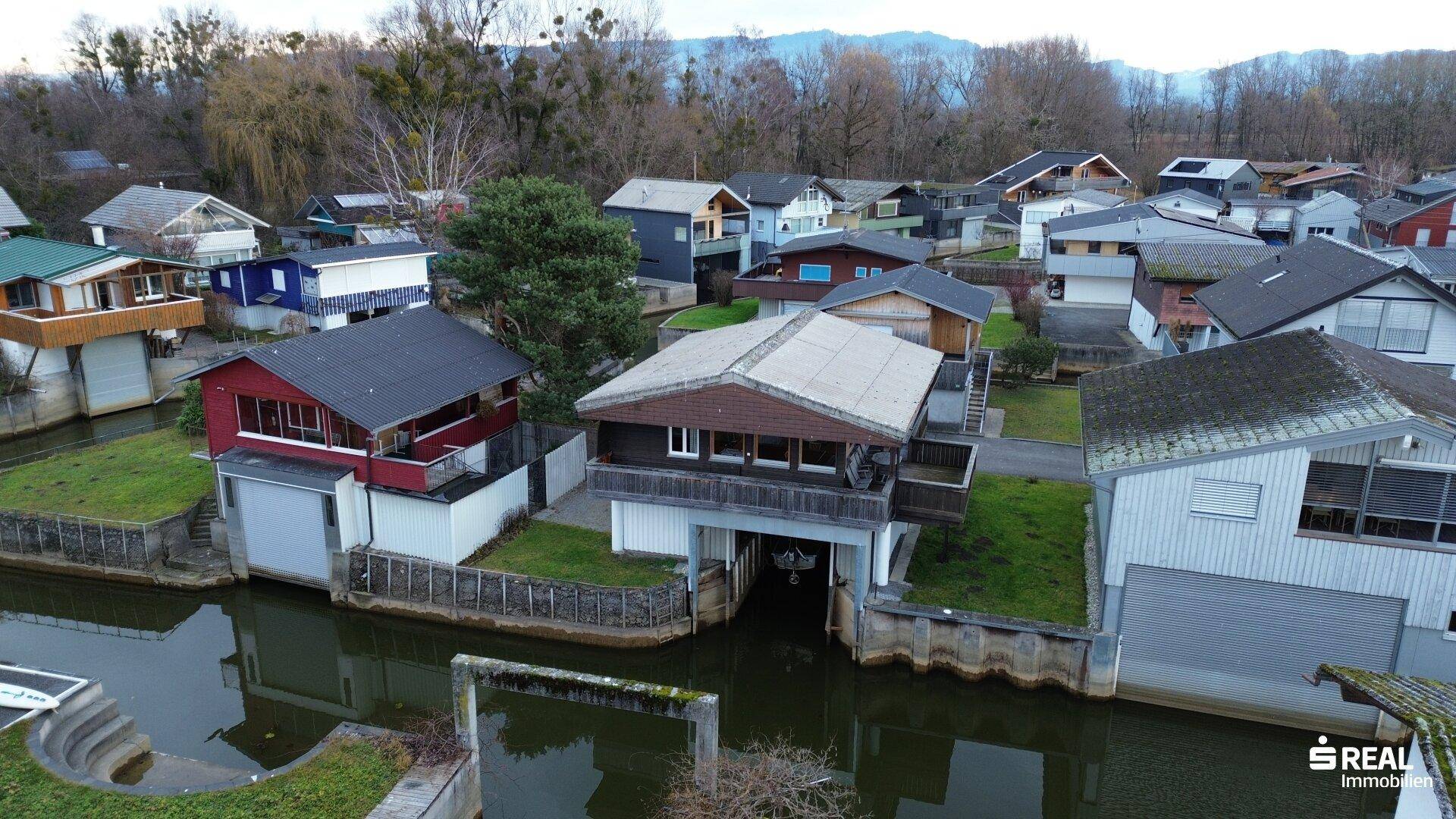 Weitläufige Luftaufnahme der Siedlung am Wasser mit vielen Häusern und Grünflächen.