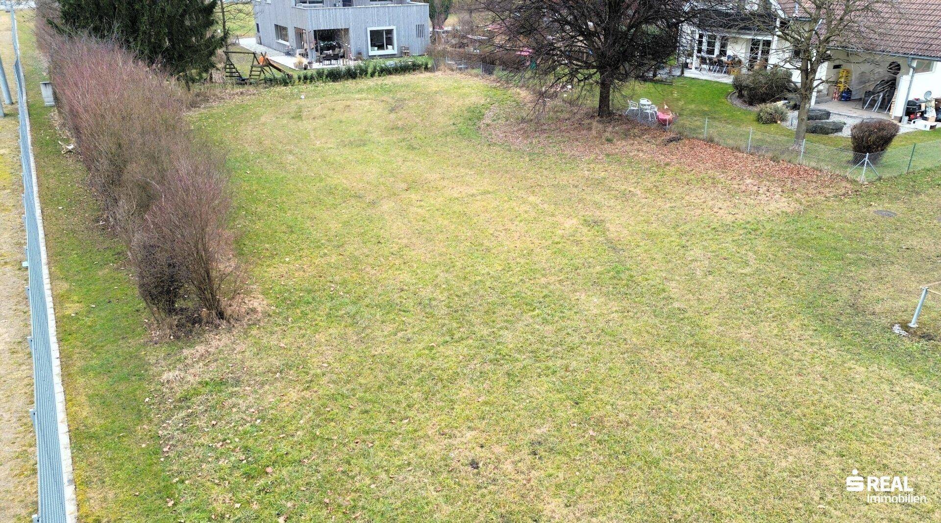 Übersicht des Grundstücks mit Rasenfläche, einer Hecke und umliegenden Wohnhäusern und Sportanlagen.