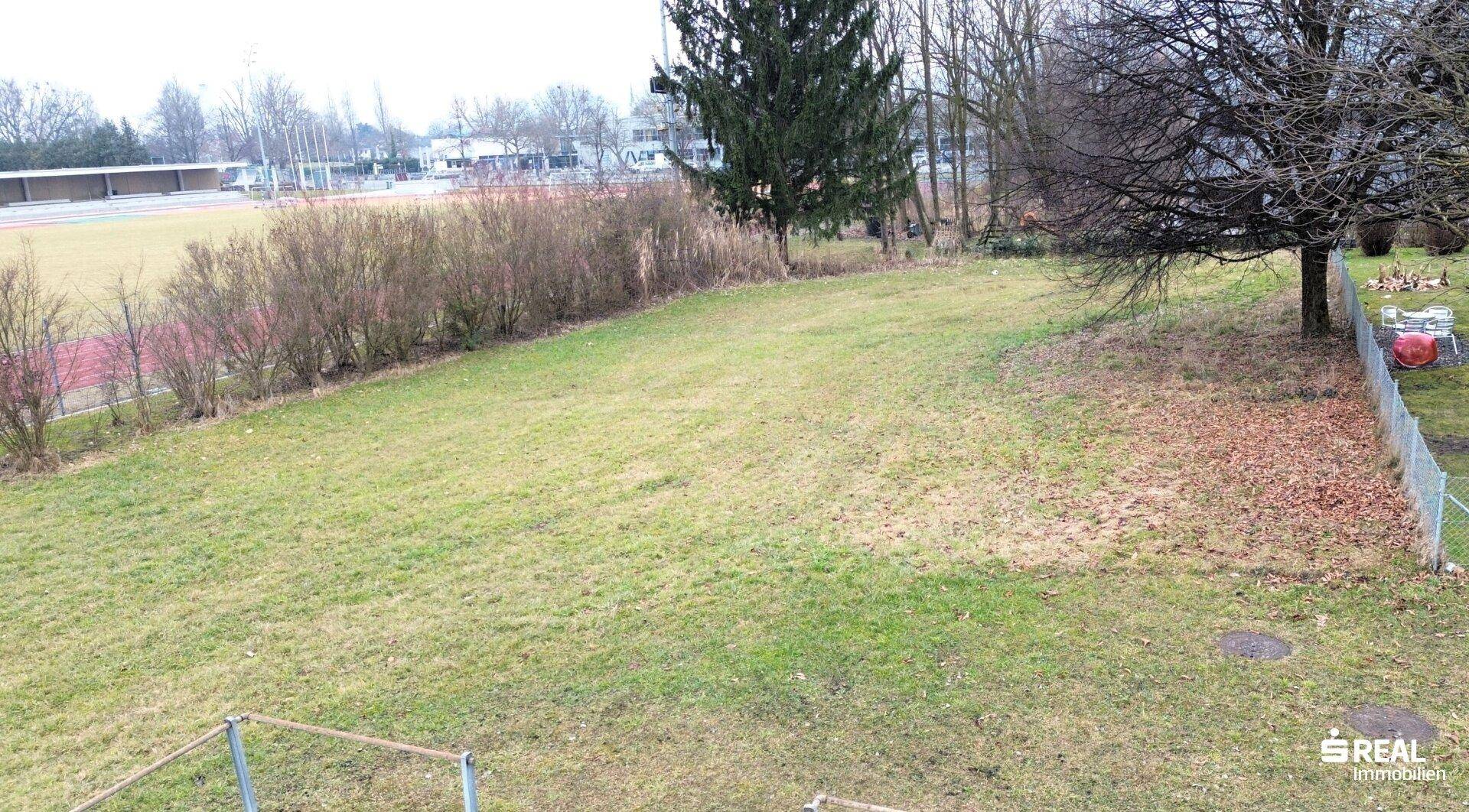 Weitläufige Grünfläche mit Blick auf eine Sportanlage und die umgebende Bebauung.