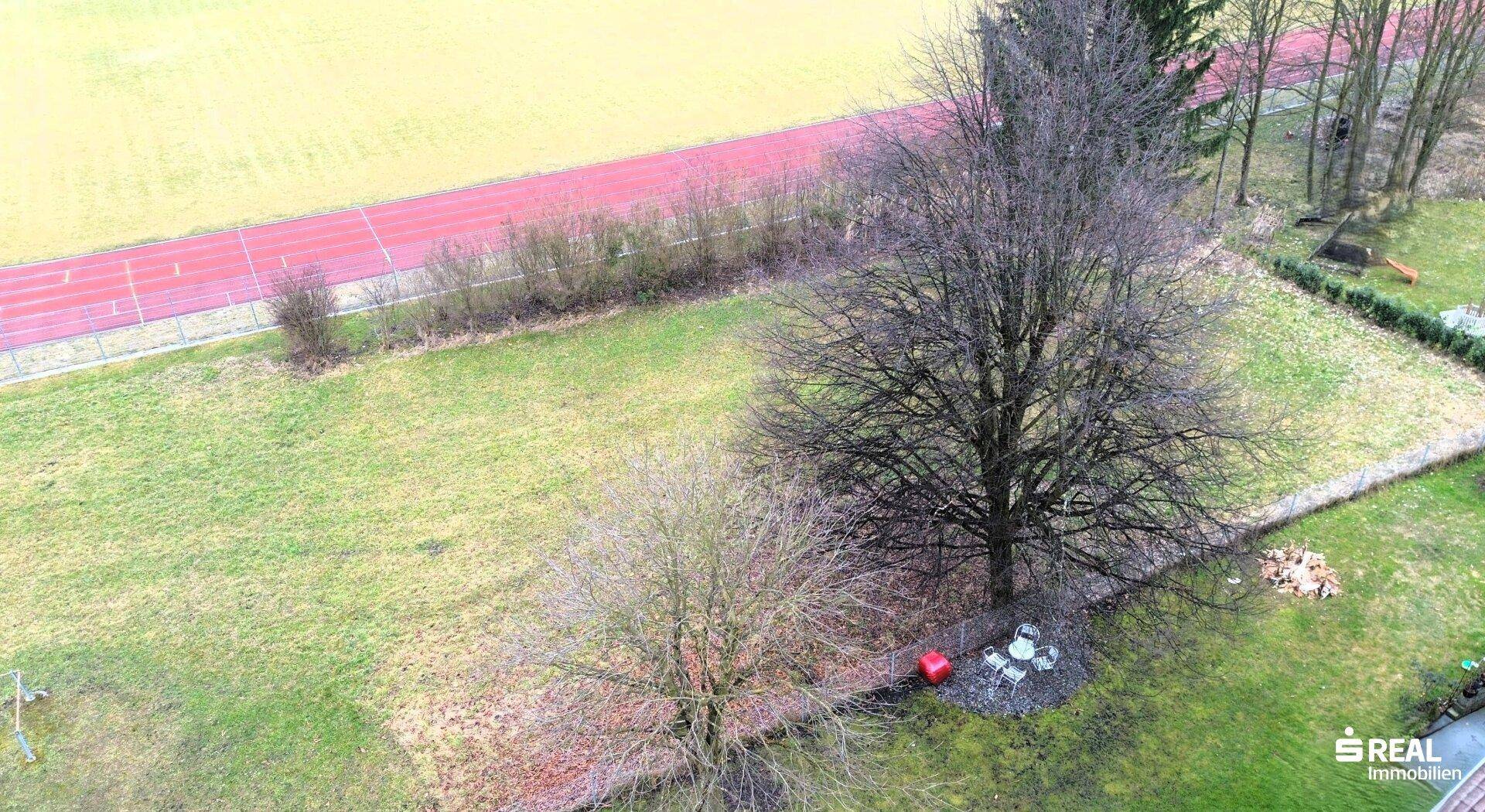Luftaufnahme eines Grundstücks mit Rasen, Bäumen und einer kleinen Sitzgelegenheit im Freien.