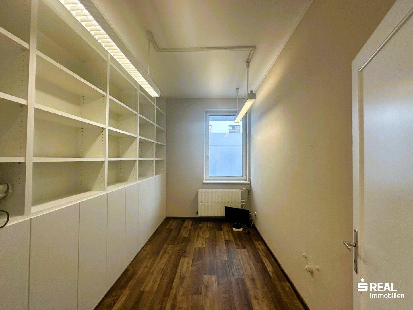 Raum mit eingebauten Regalen, Holzboden und einem Fenster, geeignet als Büro oder Archiv.