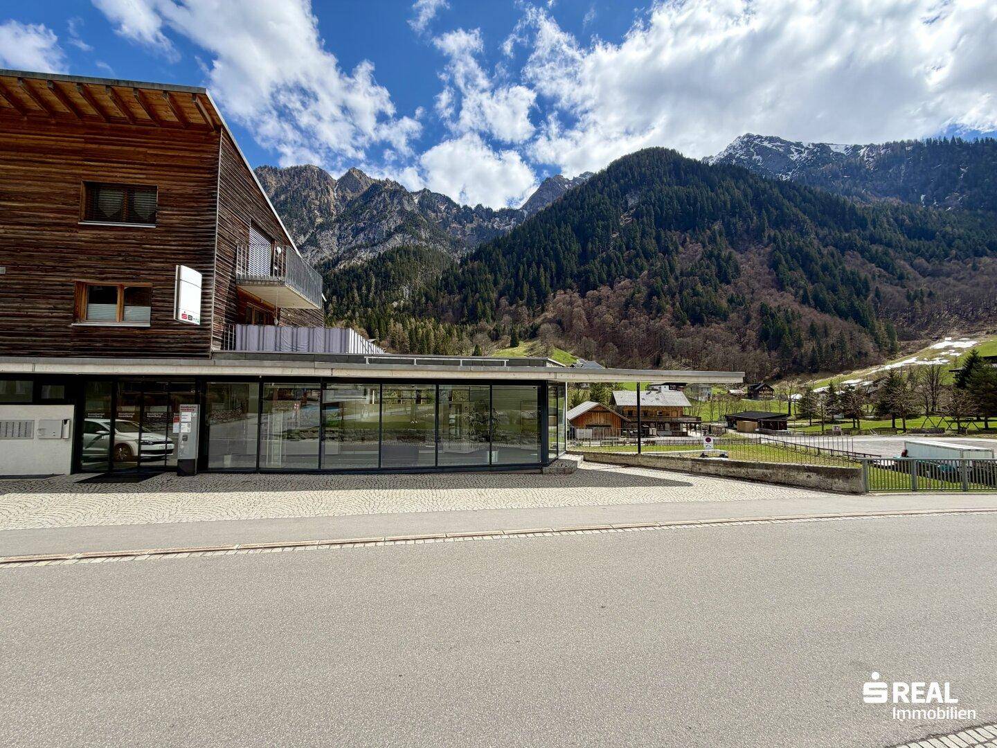 Ansicht des modernen Gebäudes mit Holzverkleidung und weitem Blick auf die umliegenden Berge und grüne Landschaft.