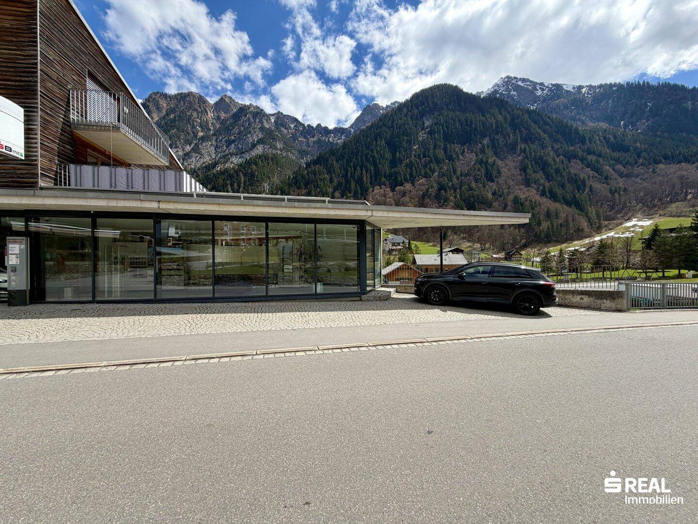 Gebäudeansicht mit moderner Architektur, Holzfassade und einem geparkten Auto davor auf dem Parkplatz.