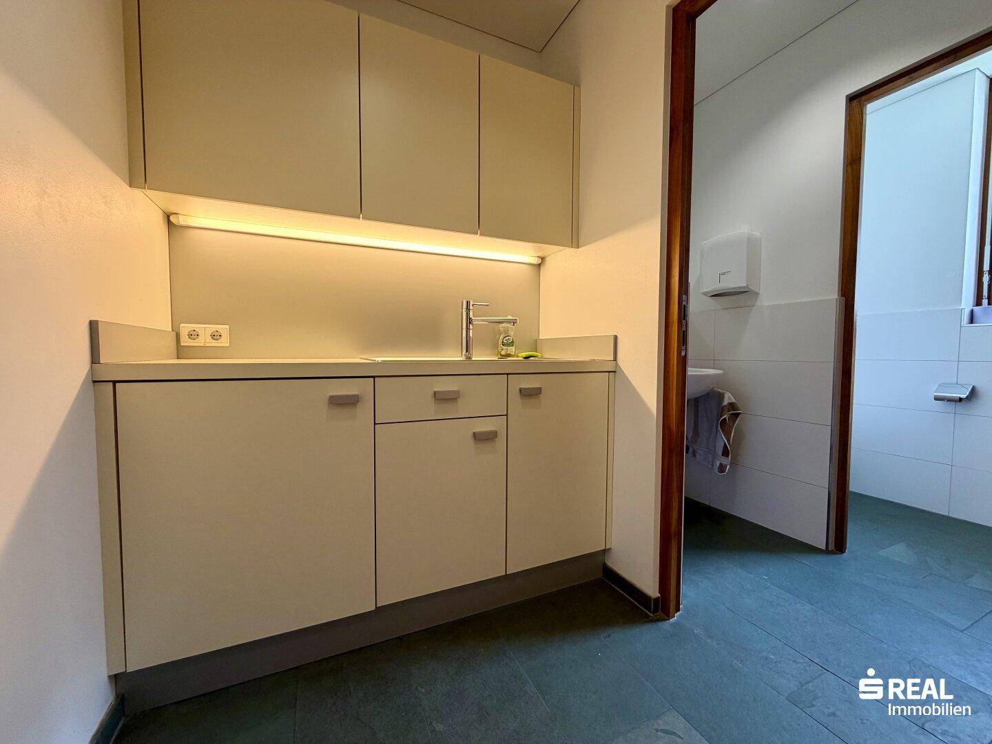 Kleine Küchenzeile mit Spüle und Unterschränken, die direkt an einen Toilettenbereich angrenzt.