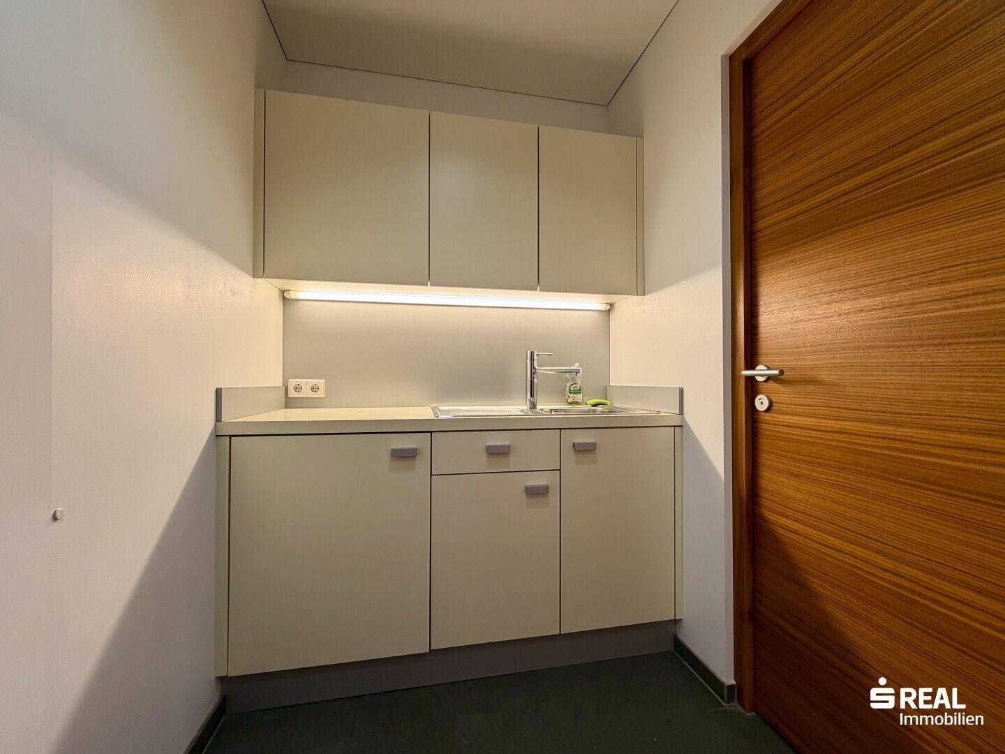 Kompakte Küchenzeile mit hellen Schränken, Spülbecken und einer modernen Holzfurniertür.