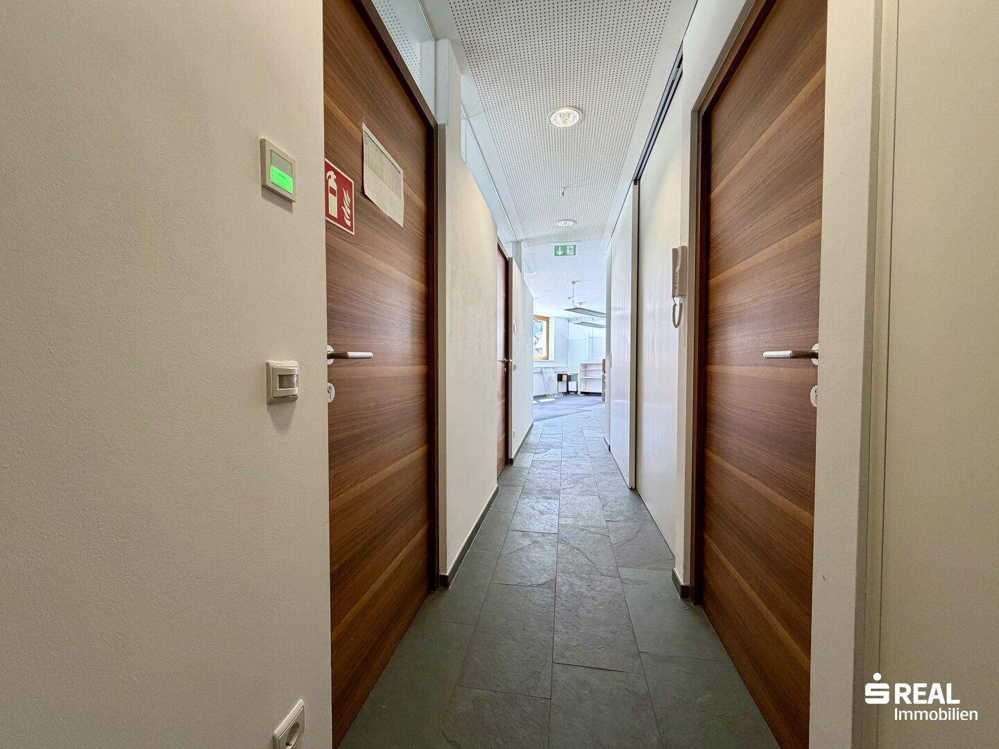 Heller Flur mit modernen Holzfurniertüren und einem Blick in einen weiteren Bürobereich.