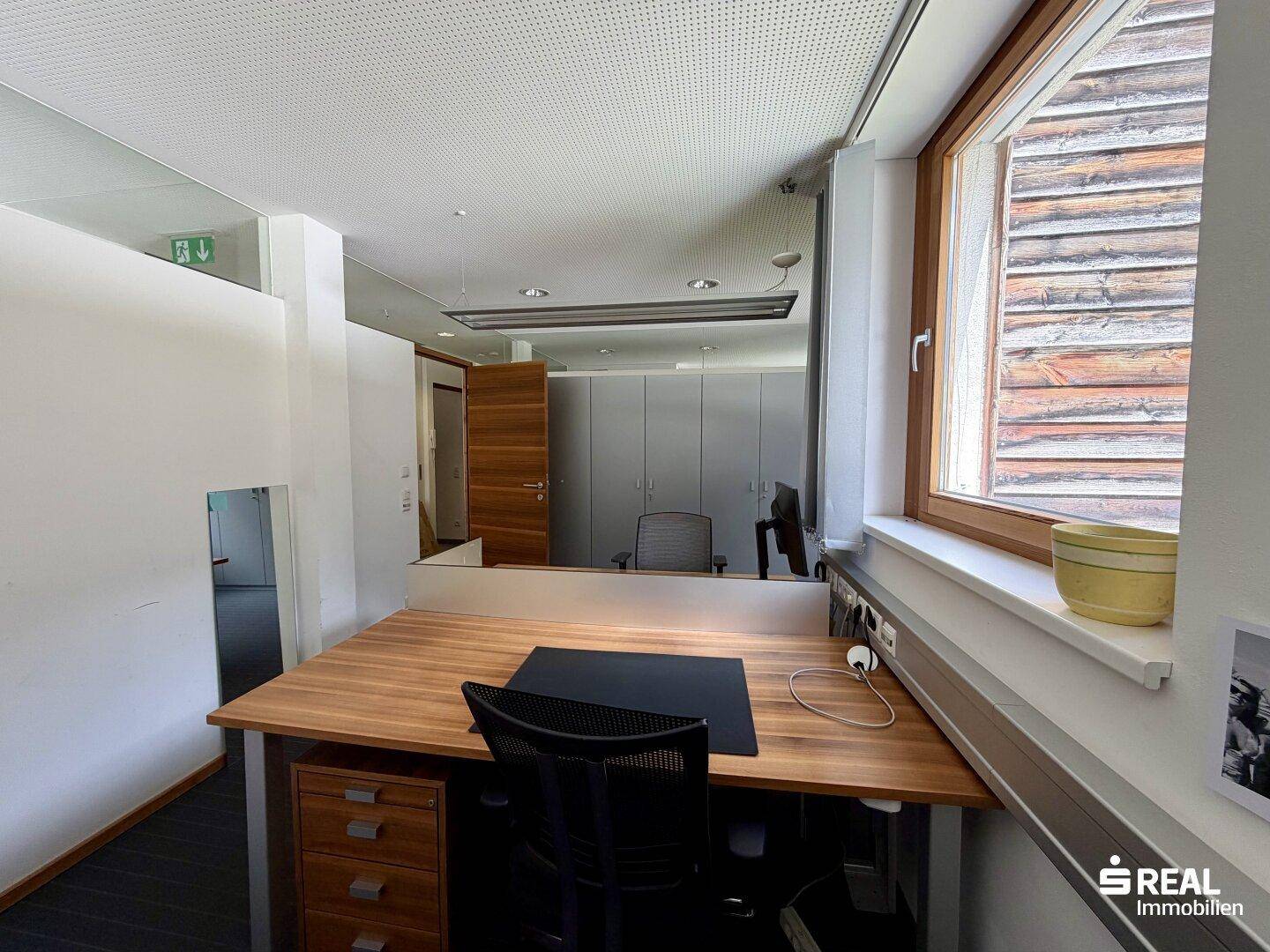 Helles Büro mit einem Holzschreibtisch, ergonomischem Stuhl und einem Fenster mit Blick ins Grüne.