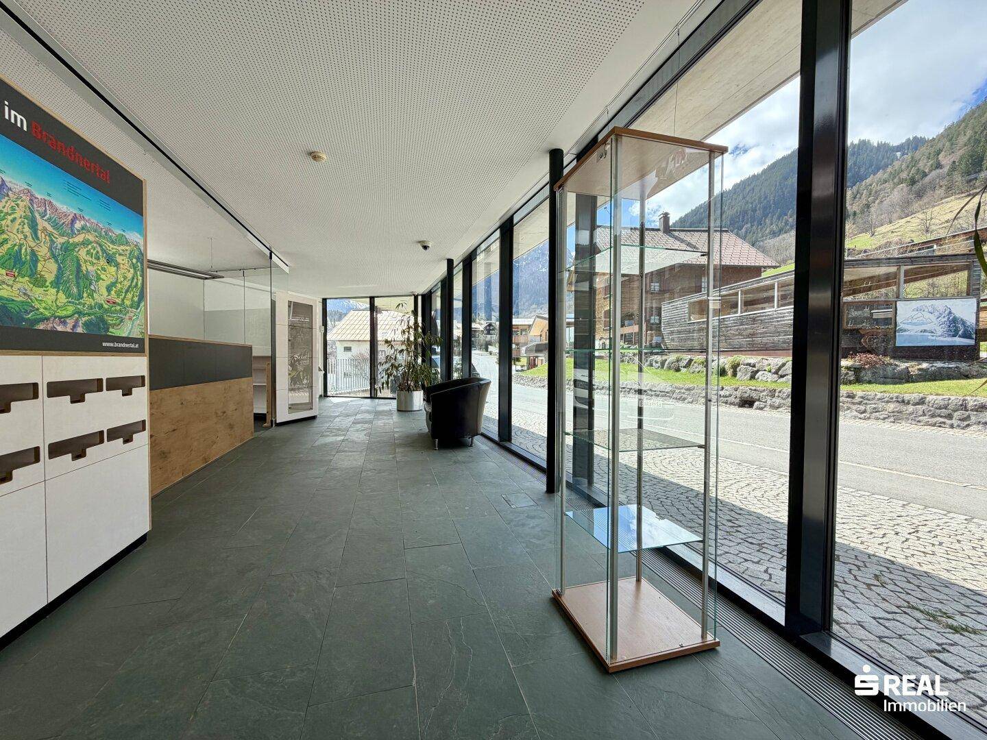 Heller Empfangsbereich mit großen Glasfronten, die einen weiten Blick auf die umliegende Berglandschaft ermöglichen.