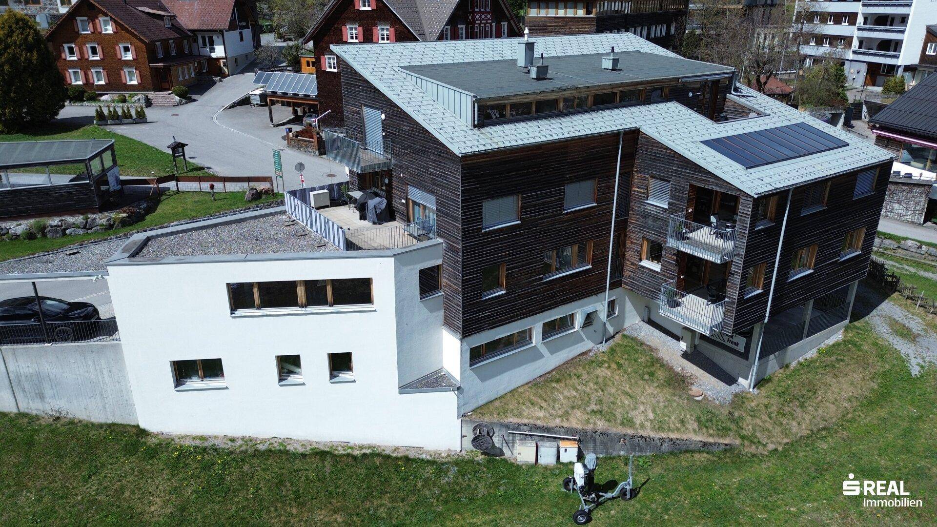 Luftaufnahme des modernen Gebäudes mit Holzfassade, Balkonen und einer Solaranlage auf dem Dach.