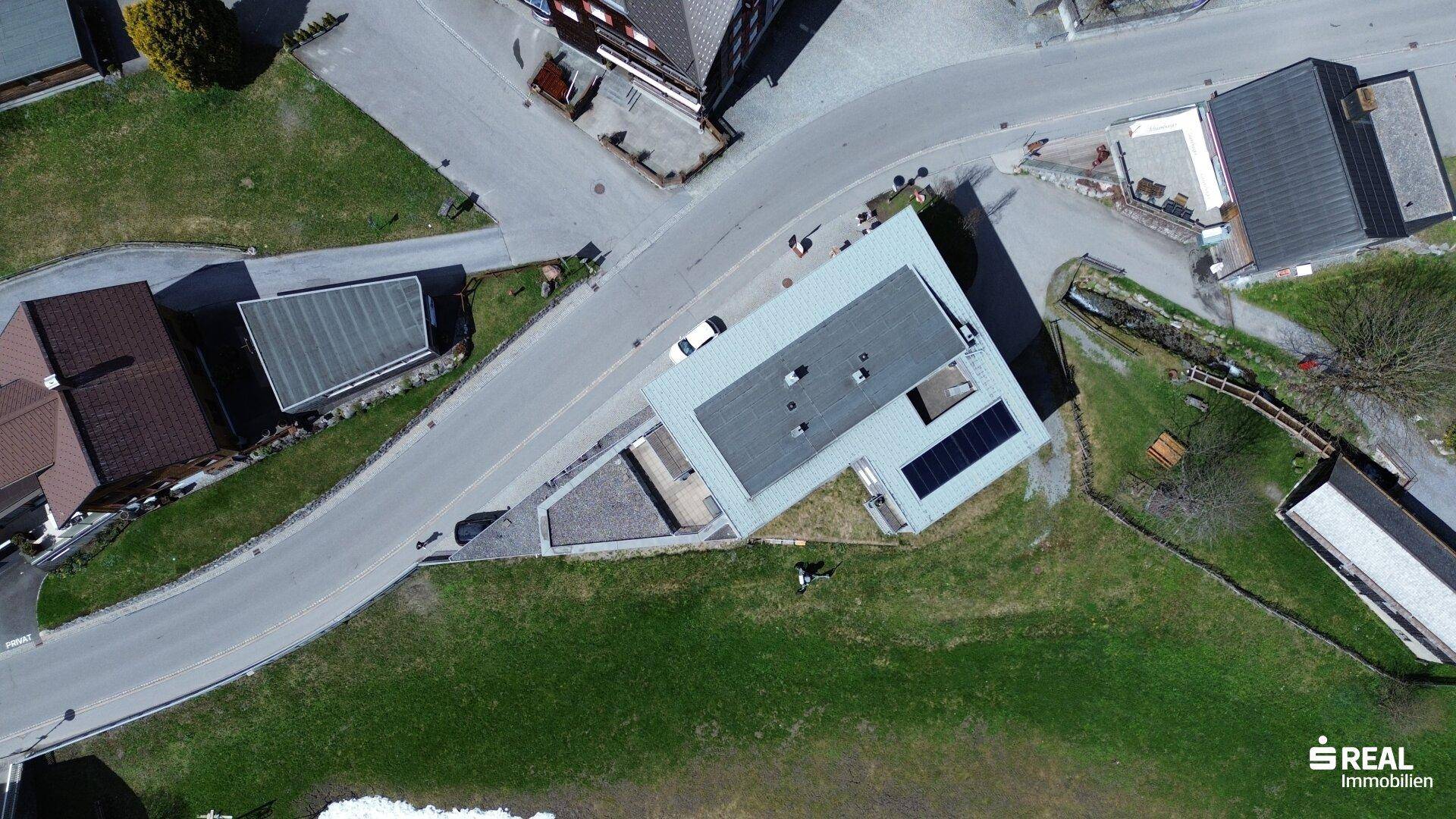 Vogelperspektive des Gebäudes mit Flachdach, Solarpaneelen und umliegenden Straßen und Grünflächen.