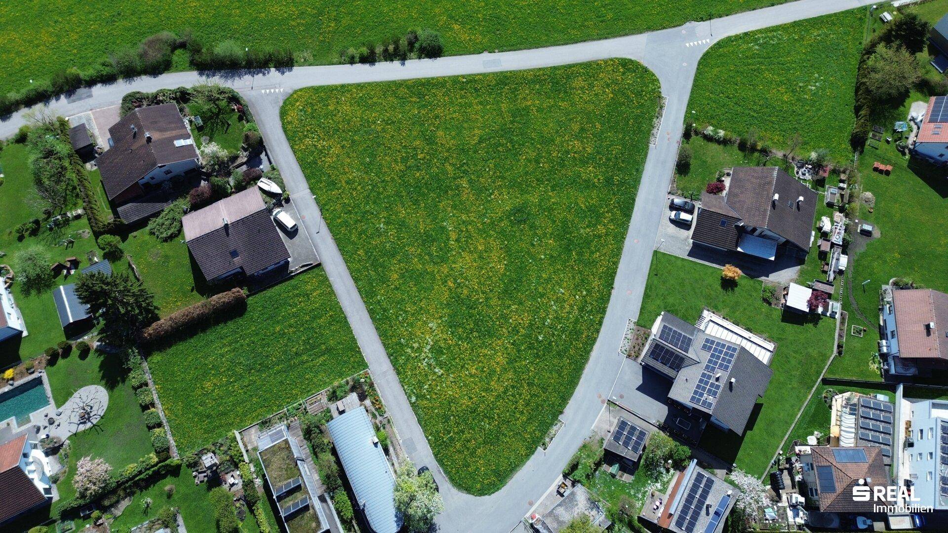 Dreieckiges unbebautes Grundstück aus der Vogelperspektive, umgeben von Einfamilienhäusern und Straßen.