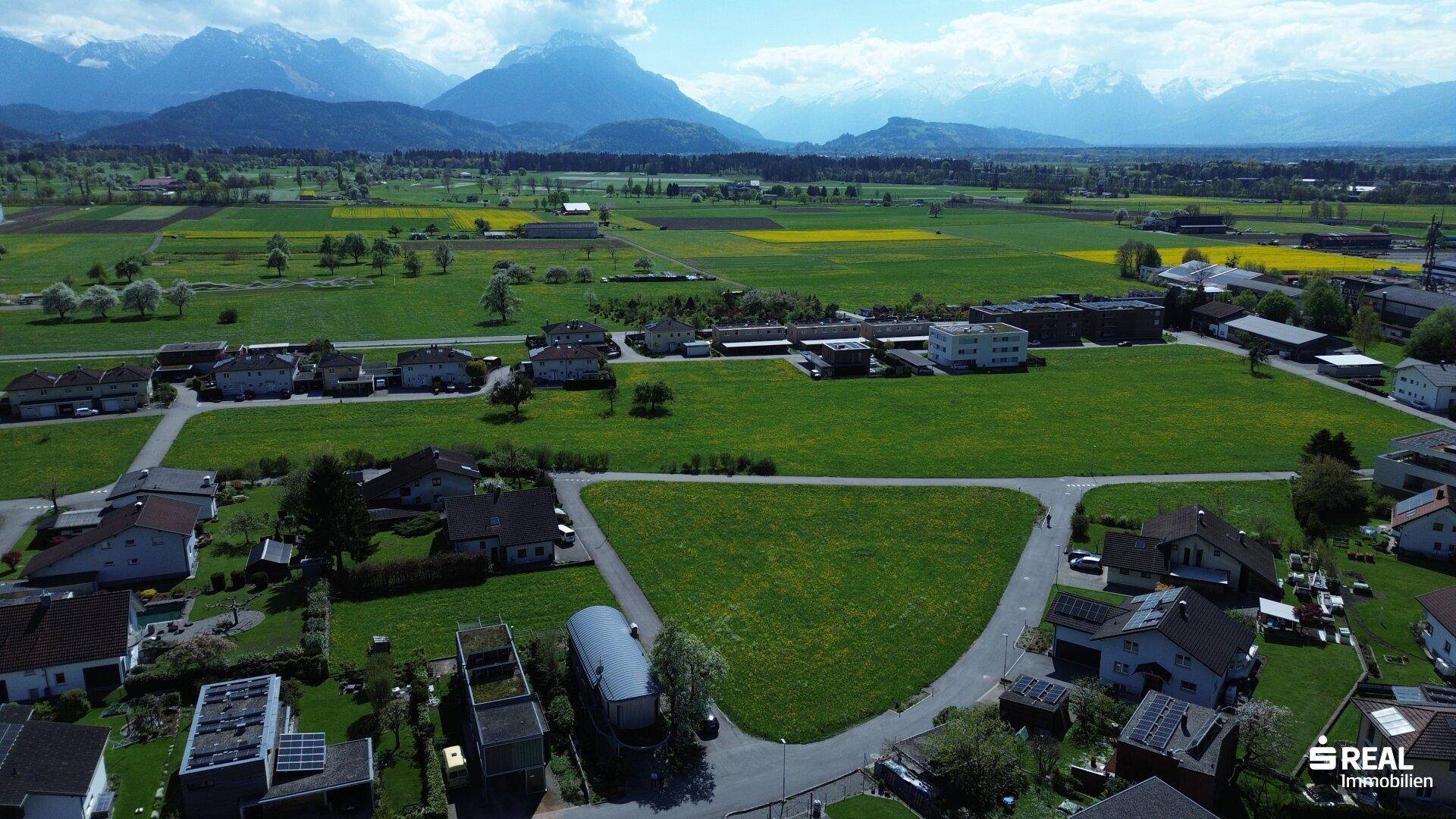 Panoramablick aus der Luft auf das Grundstück, umgeben von Häusern, Feldern und einer beeindruckenden Bergkulisse.