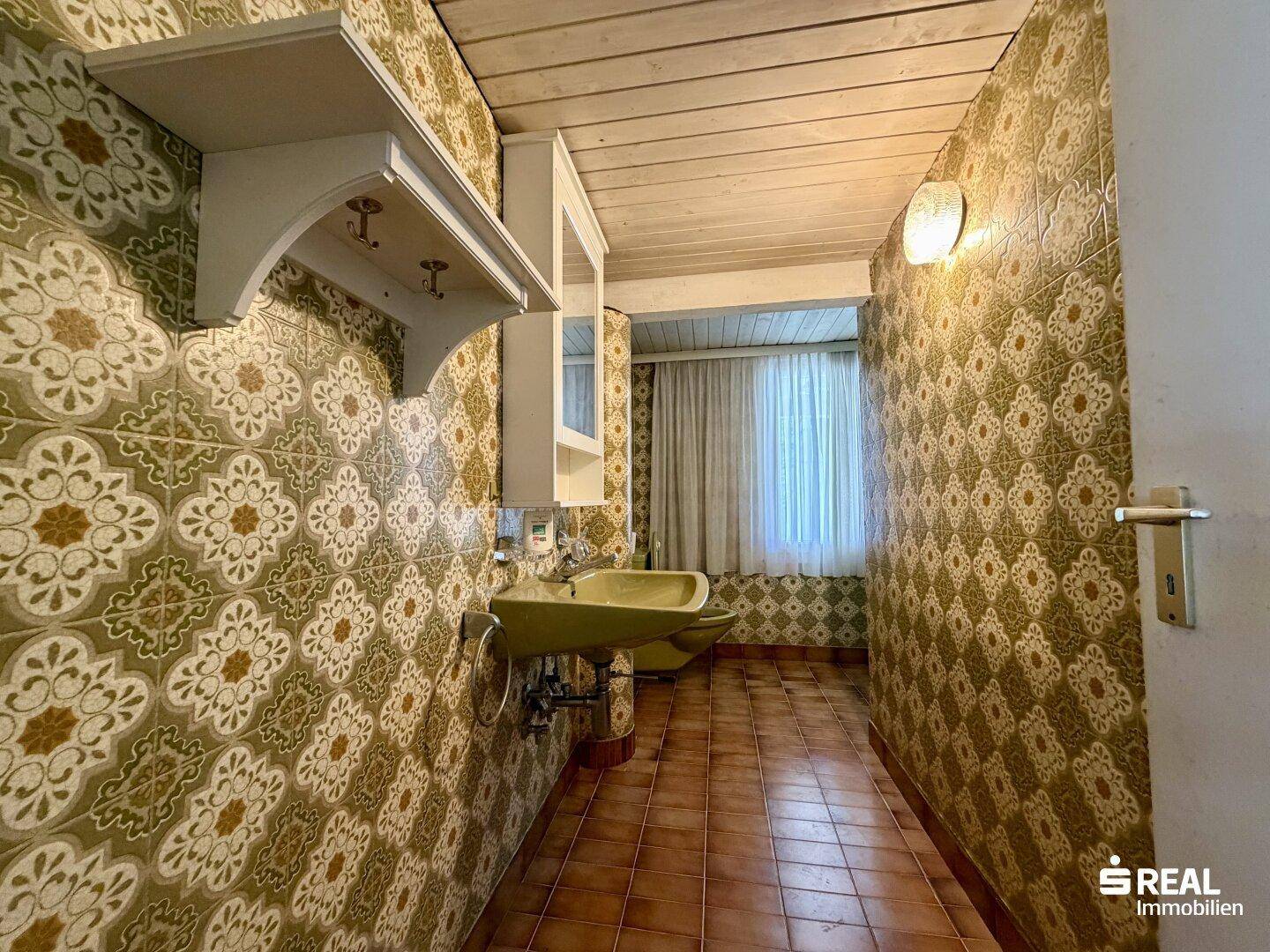 Badezimmer mit gemusterten Fliesen, Waschtisch und Fenster.