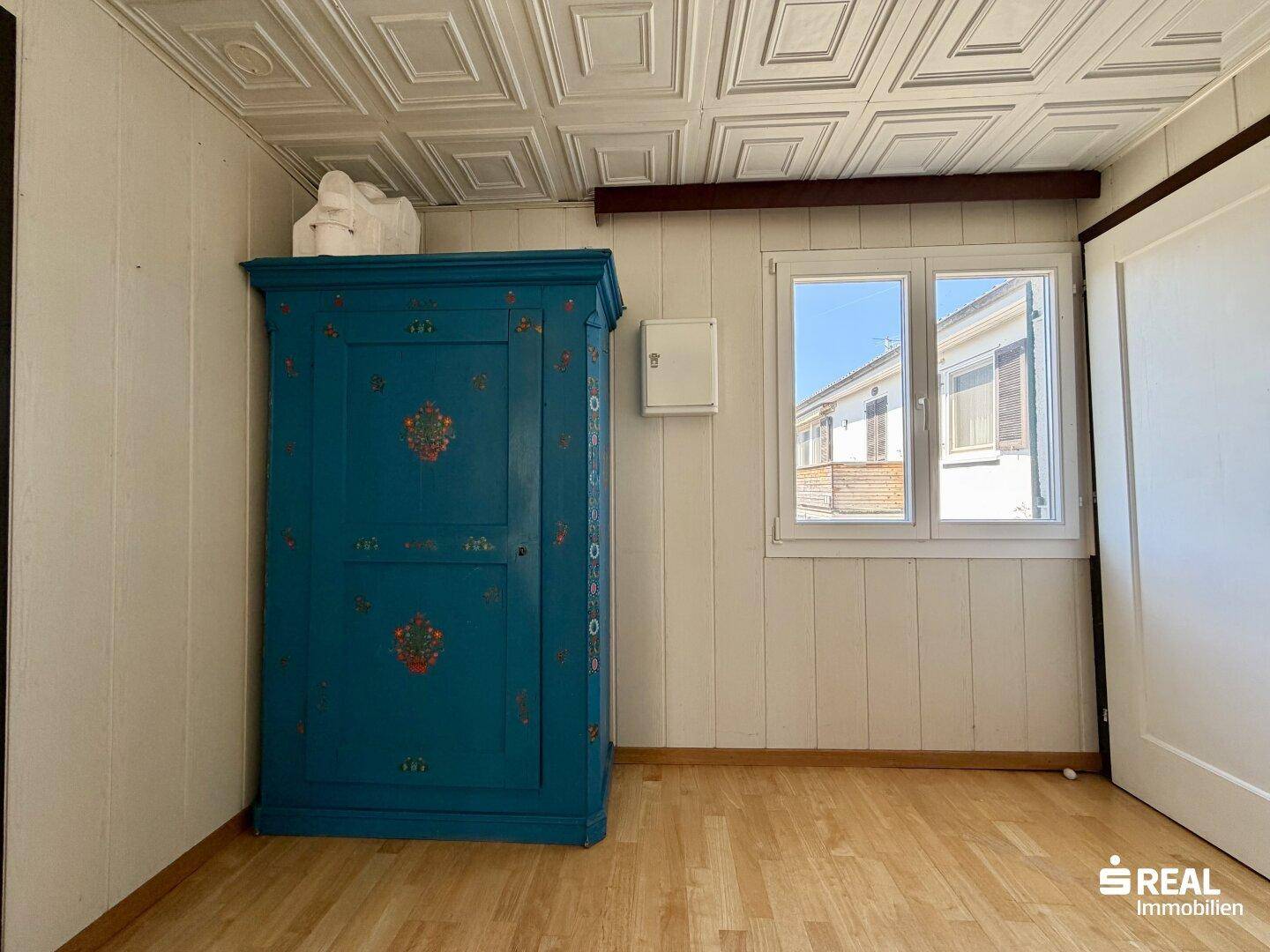 Schlafzimmer mit Holzboden, weiß getäfelten Wänden und farbigem Schrank.