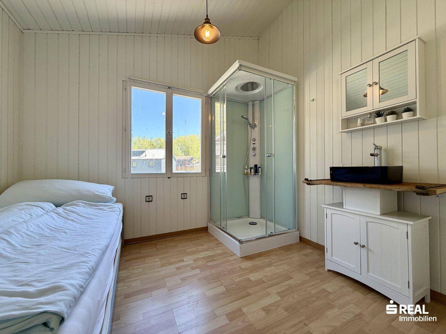 Schlafzimmer mit Holzboden, Duschkabine und Waschtisch.