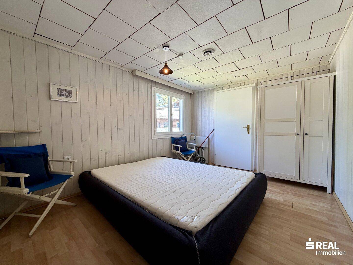 Schlafzimmer mit Doppelbett, Holzboden und weiß getäfelten Wänden.