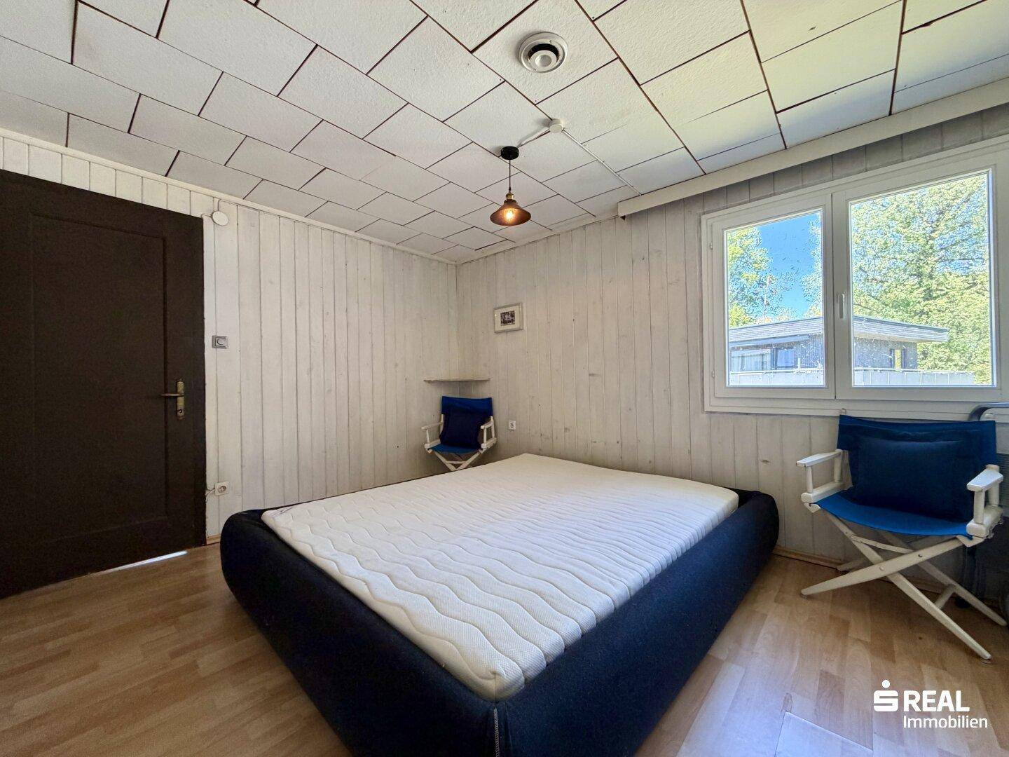 Helles Schlafzimmer mit Holzboden und Fenster mit Blick ins Grüne.