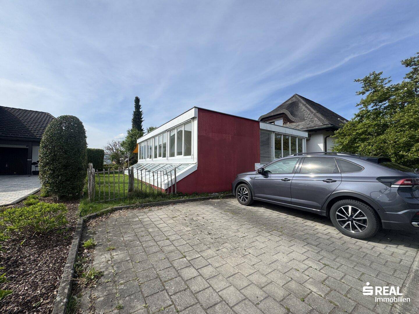 Außenansicht des Gebäudes mit gepflastertem Parkplatz und angrenzendem Gartenbereich.