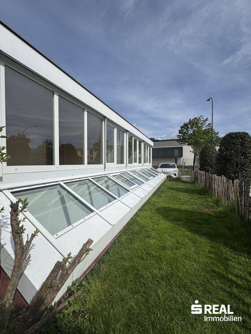 Moderne Gebäudefassade mit großen Fensterfronten und schrägen Dachfenstern im Erdgeschoss.