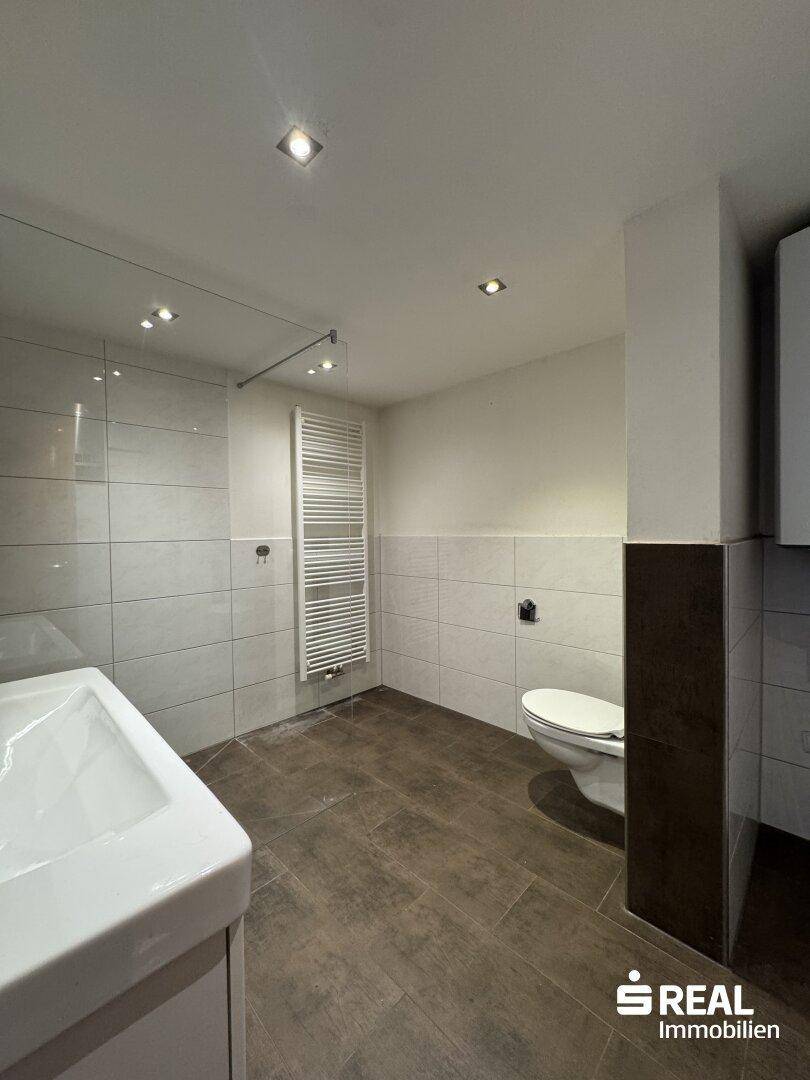 Modern gefliestes Badezimmer mit Dusche, Waschbecken und Wand-WC.