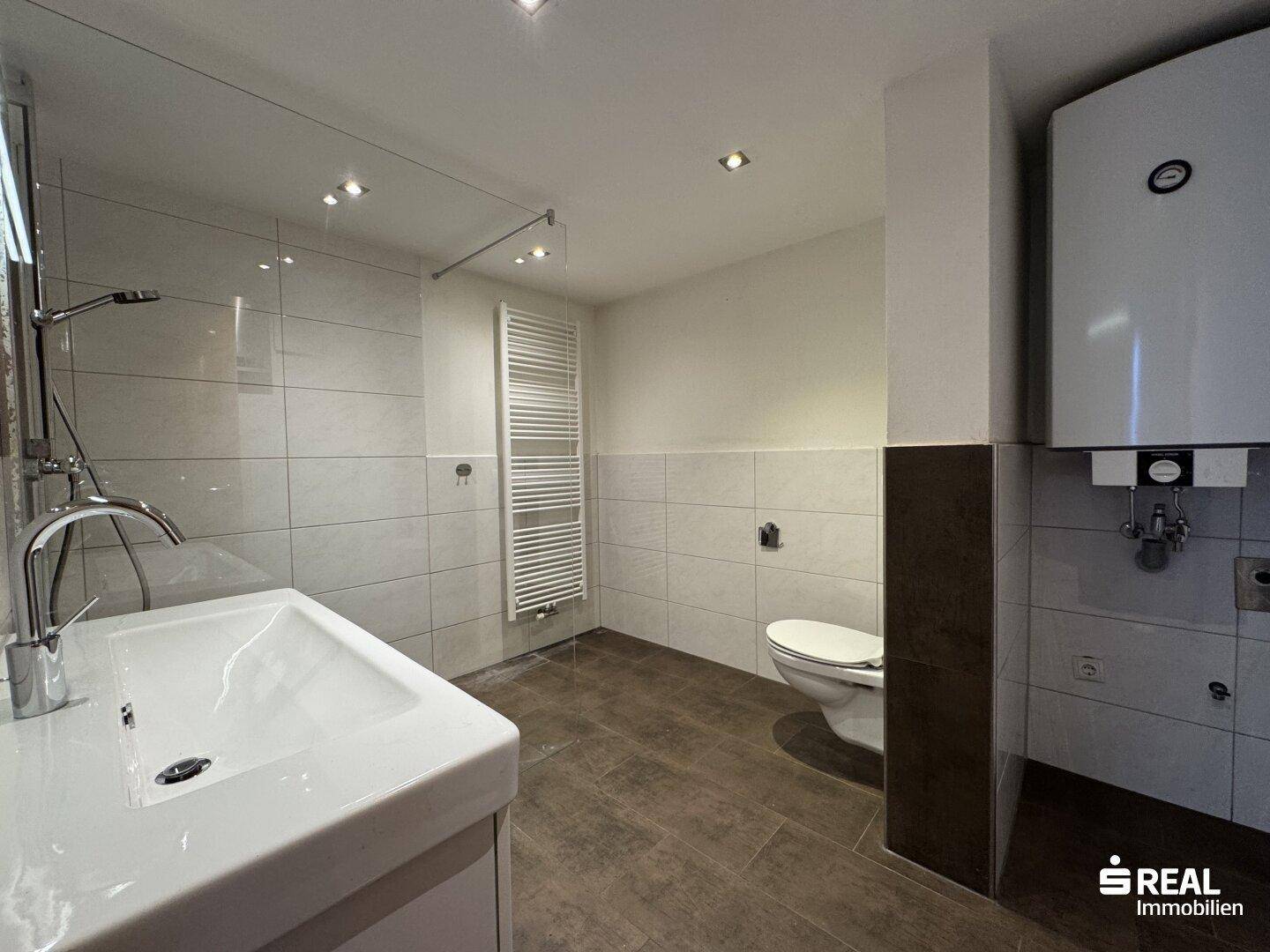 Helles Badezimmer mit moderner Dusche, Waschbecken und Boiler an der Wand.