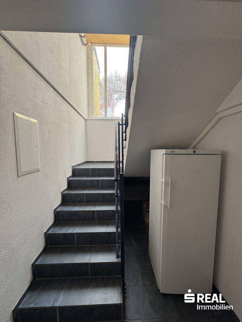 Treppenhaus mit gefliestem Boden und einem Kühlschrank im unteren Bereich.