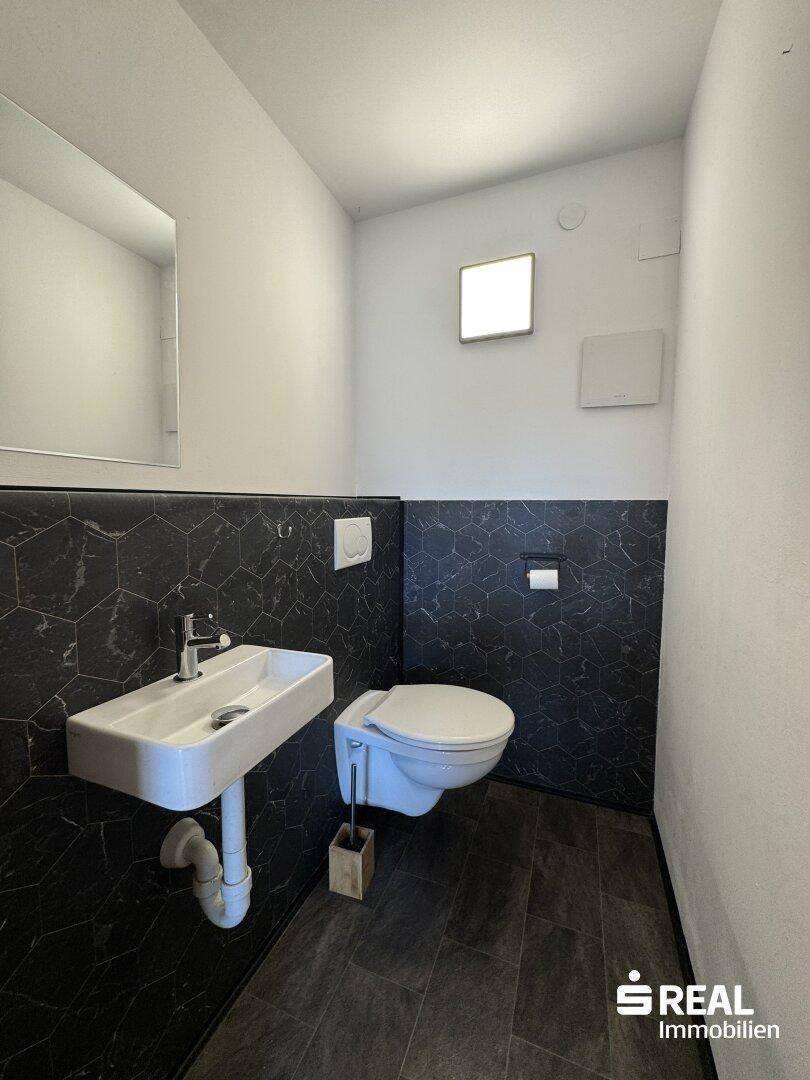 Modernes Gäste-WC mit dunklen sechseckigen Fliesen und wandhängendem WC.