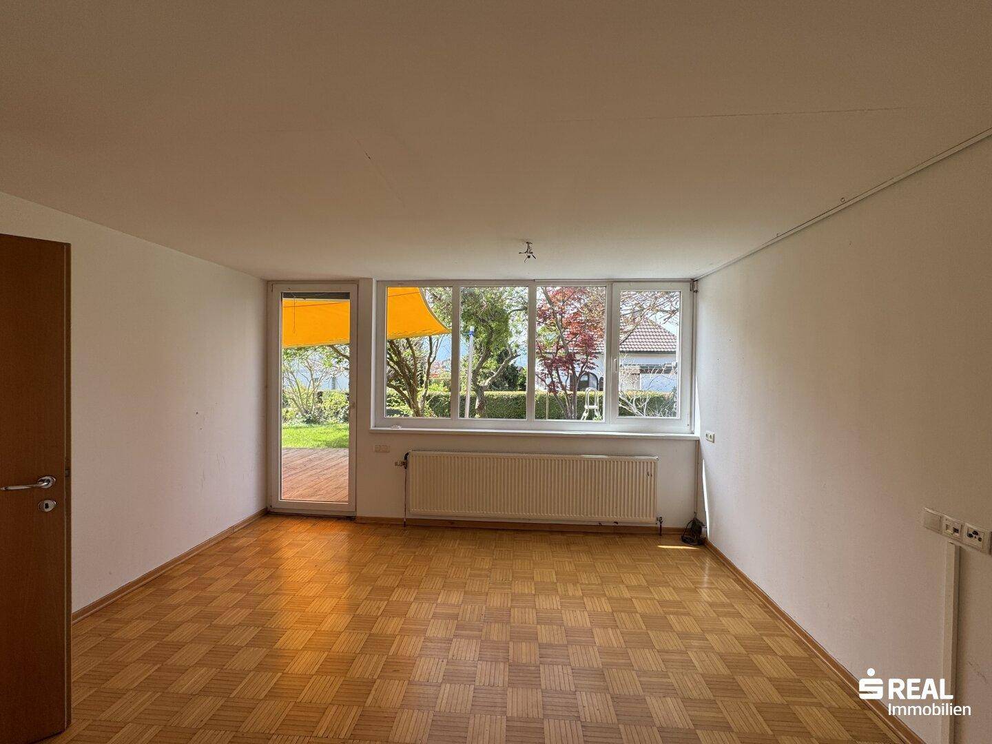 Helles Wohnzimmer mit Parkettboden und Zugang zum Garten durch eine große Fenstertür.