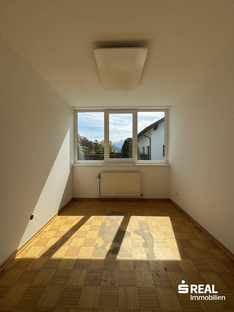 Sonniger Raum mit Parkettboden und großem Fenster, das viel Tageslicht hereinlässt.