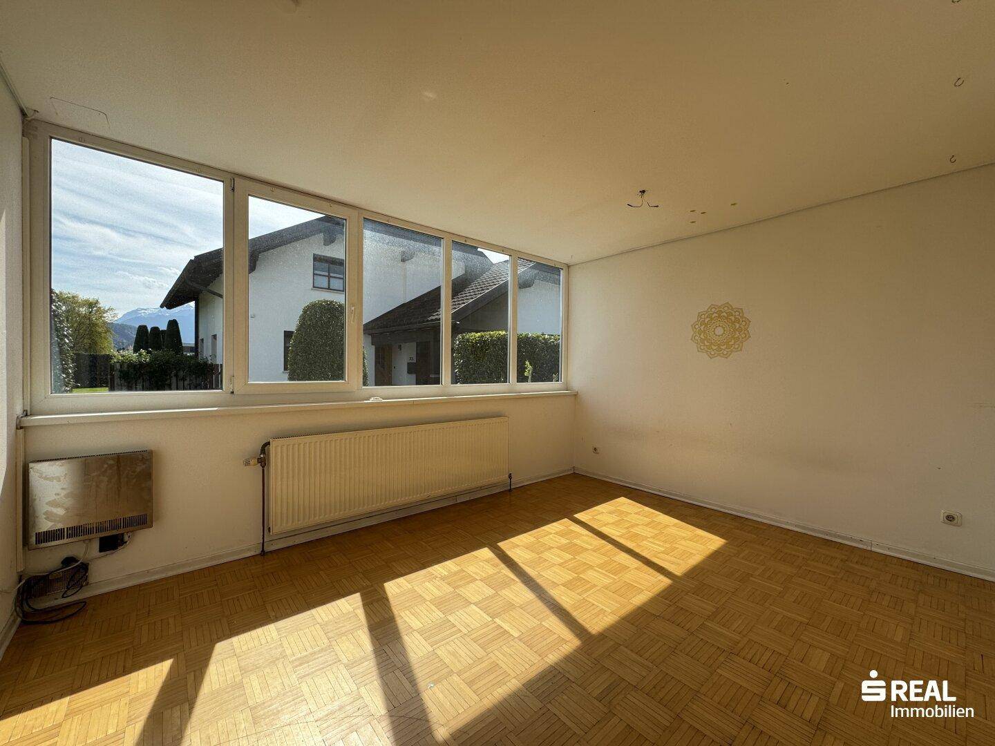 Geräumiges Wohnzimmer mit Parkettboden und breiter Fensterfront mit Blick ins Grüne.