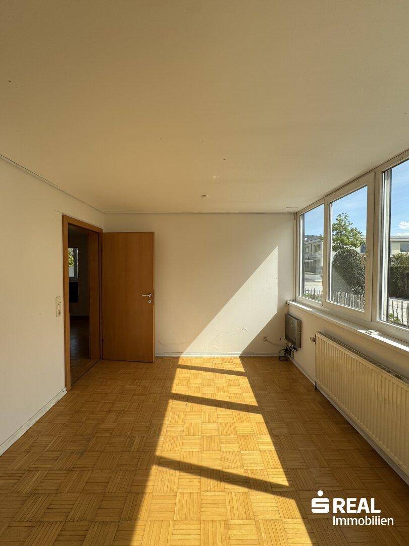 Lichtdurchfluteter Wohnbereich mit Parkettboden und großen Fenstern, die den Raum erhellen.