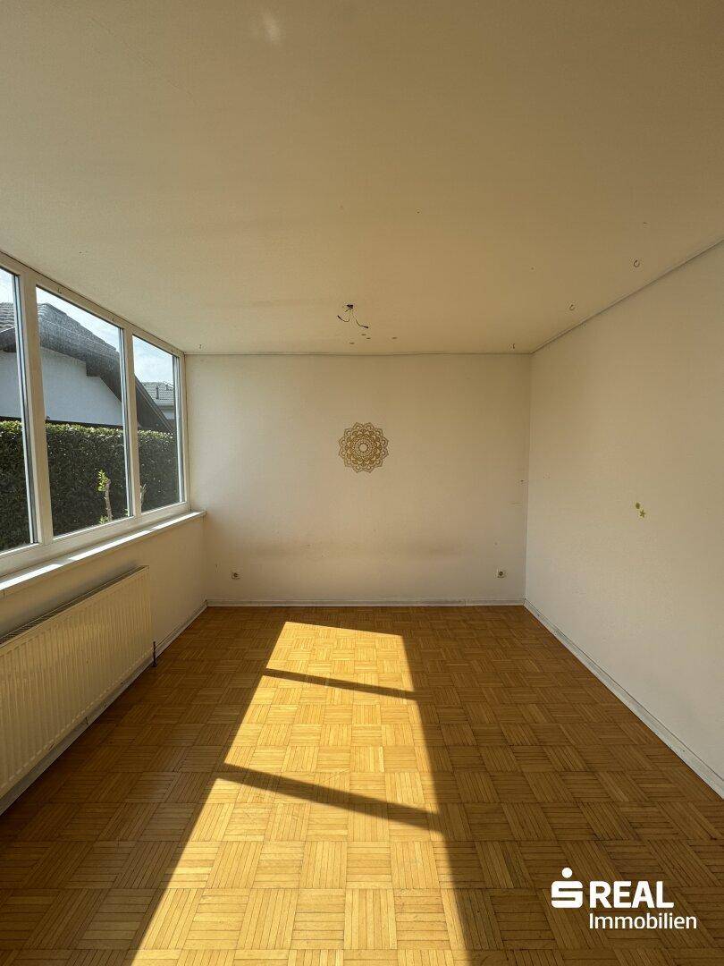 Heller Wohnraum mit Parkettboden und breiter Fensterfront, die viel Sonnenlicht einfängt.