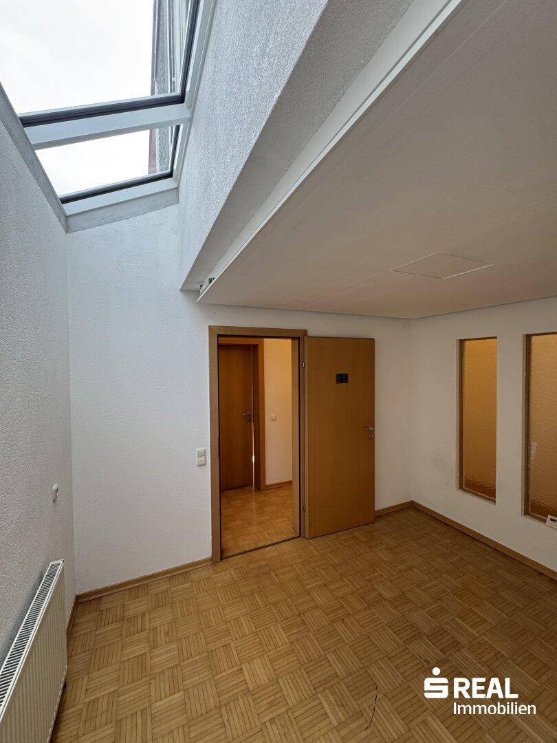 Heller Raum mit Parkettboden, Oberlicht und Zugang zu weiteren Zimmern.