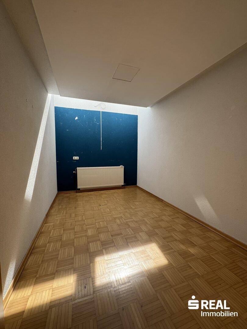 Raum mit Parkettboden und einer farbigen Akzentwand, die viel Tageslicht erhält.