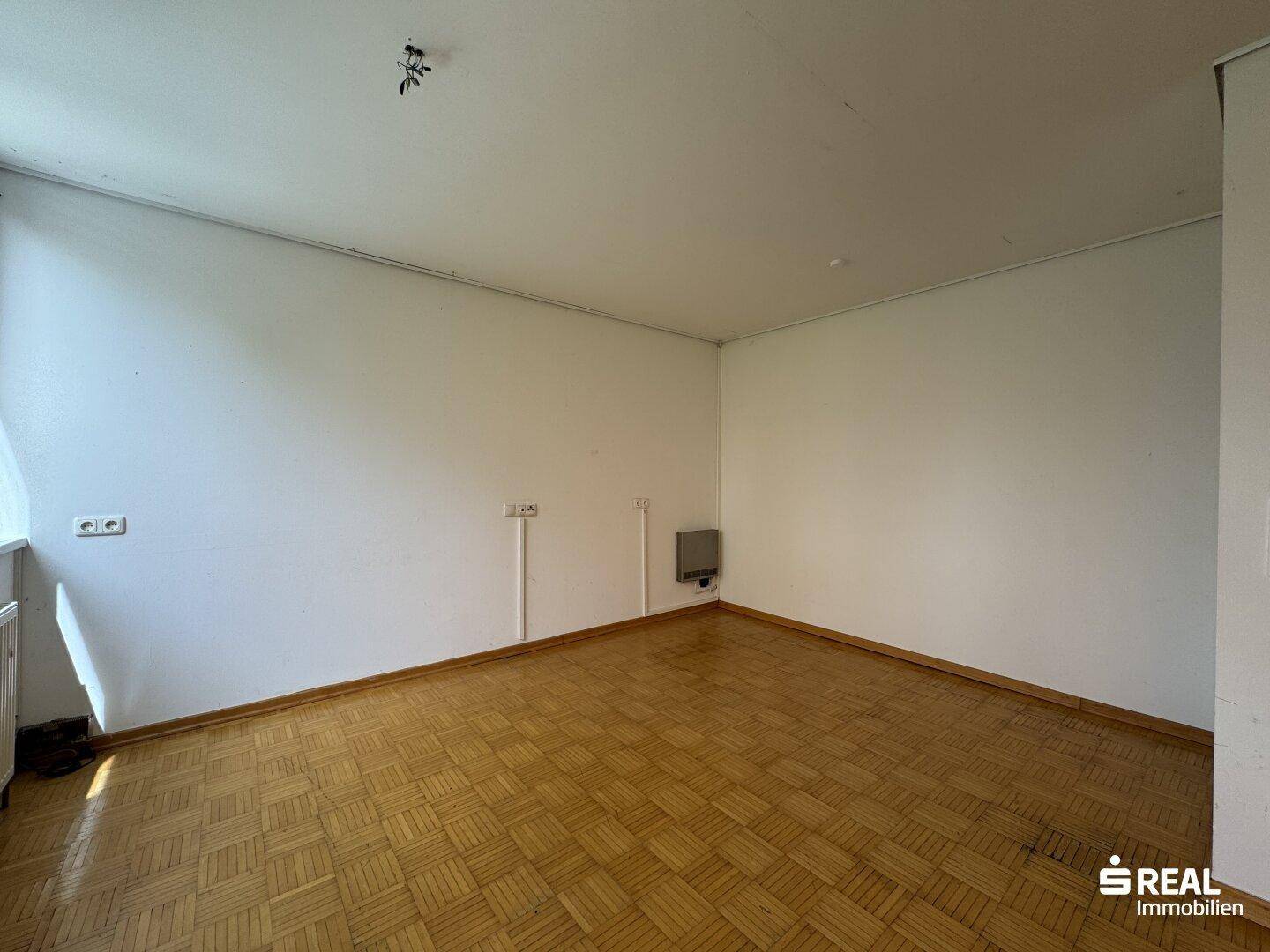 Geräumiger Raum mit Parkettboden und großen Fenstern, die den Raum hell erscheinen lassen.