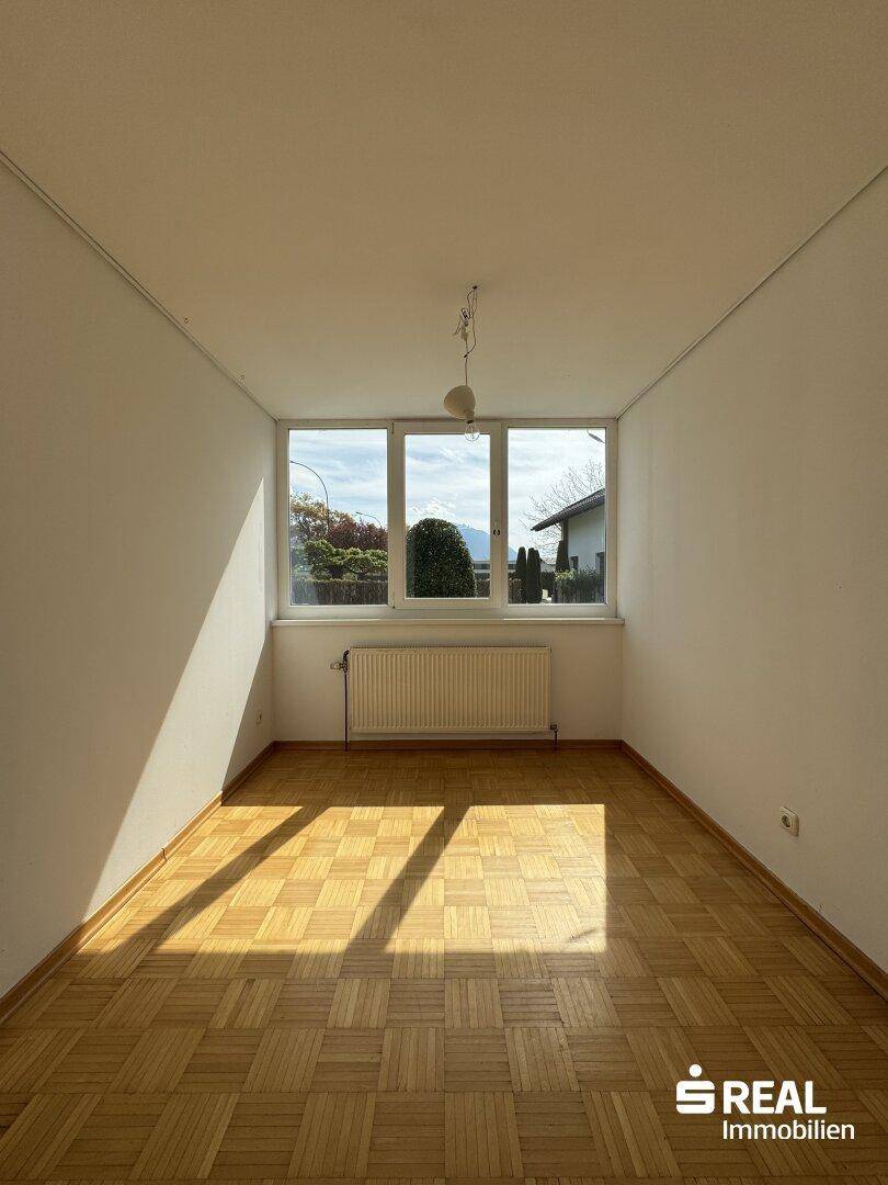 Heller Raum mit Parkettboden und großem Fenster, das viel Sonnenlicht hereinlässt.