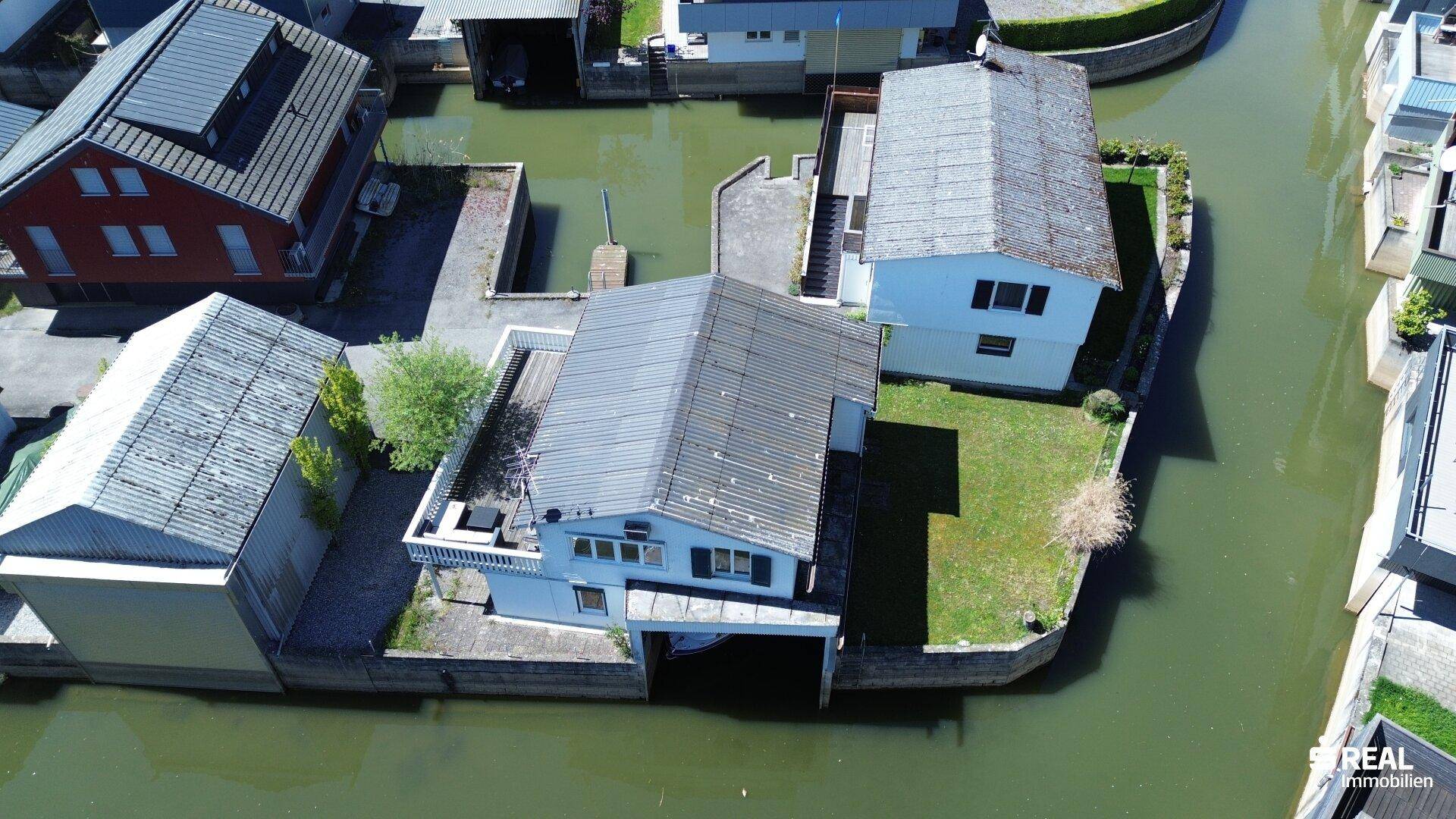 Draufsicht auf das Haus mit Bootsgarage und angrenzenden Grundstücken am Wasser.