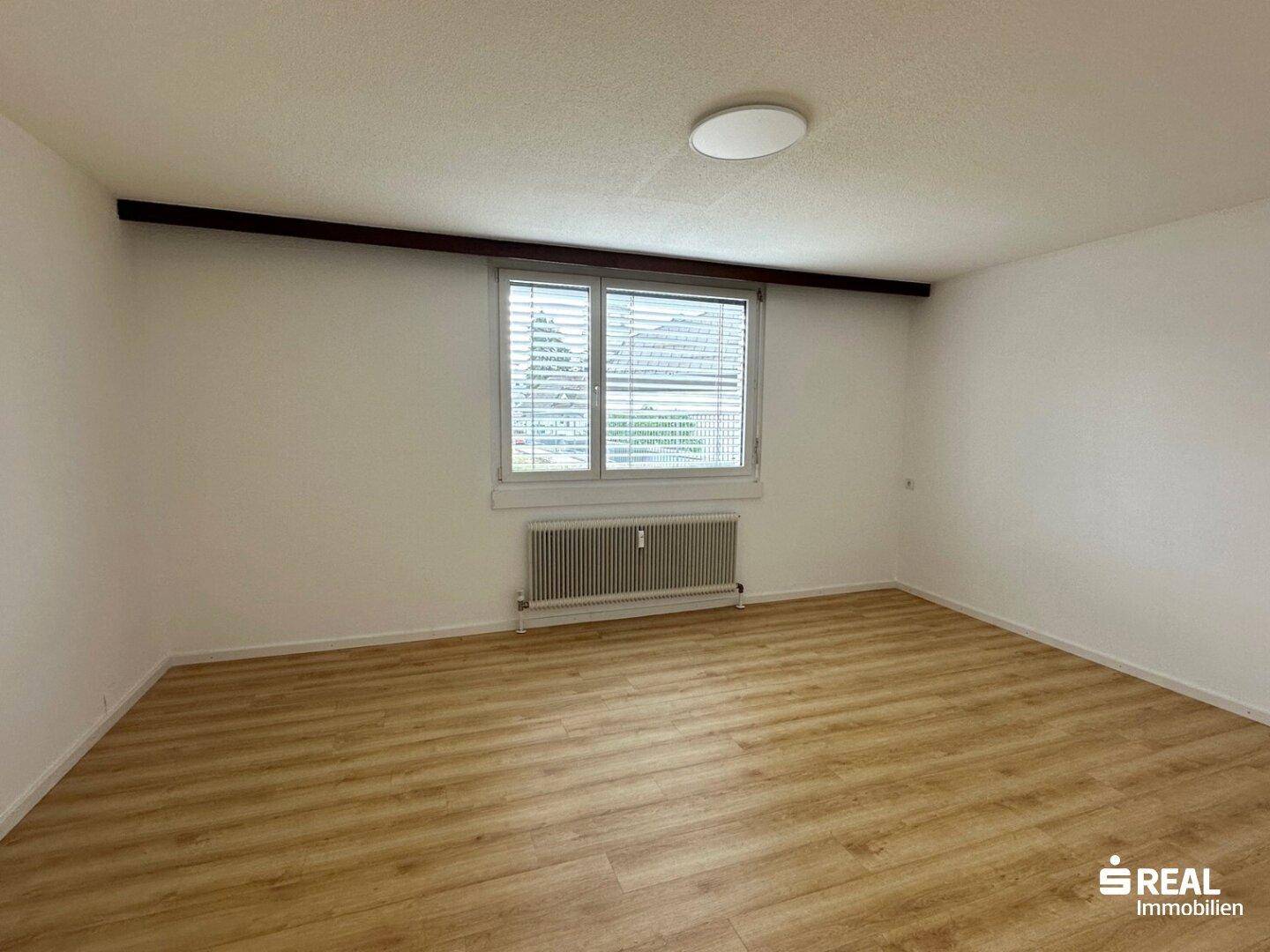 Helles Schlafzimmer mit Laminatboden und einem Fenster mit Jalousien, bereit zur Einrichtung.