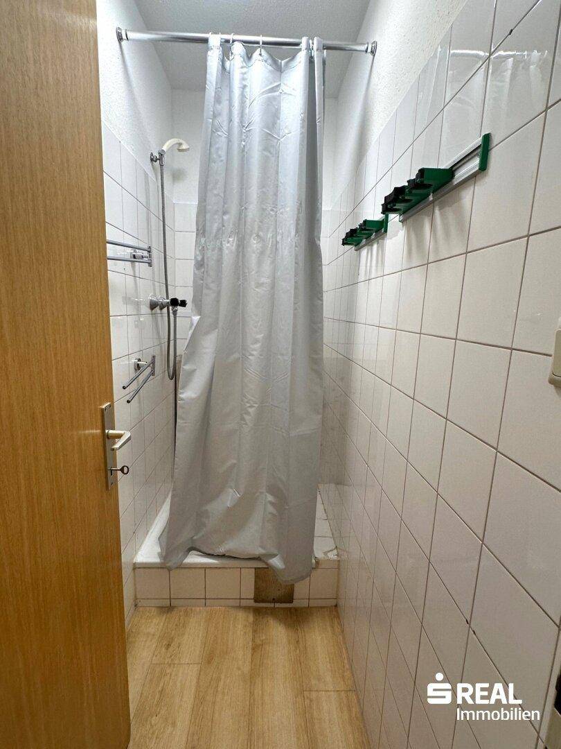 Kleines Badezimmer mit Duschwanne, weiß gefliesten Wänden und Duschvorhang.