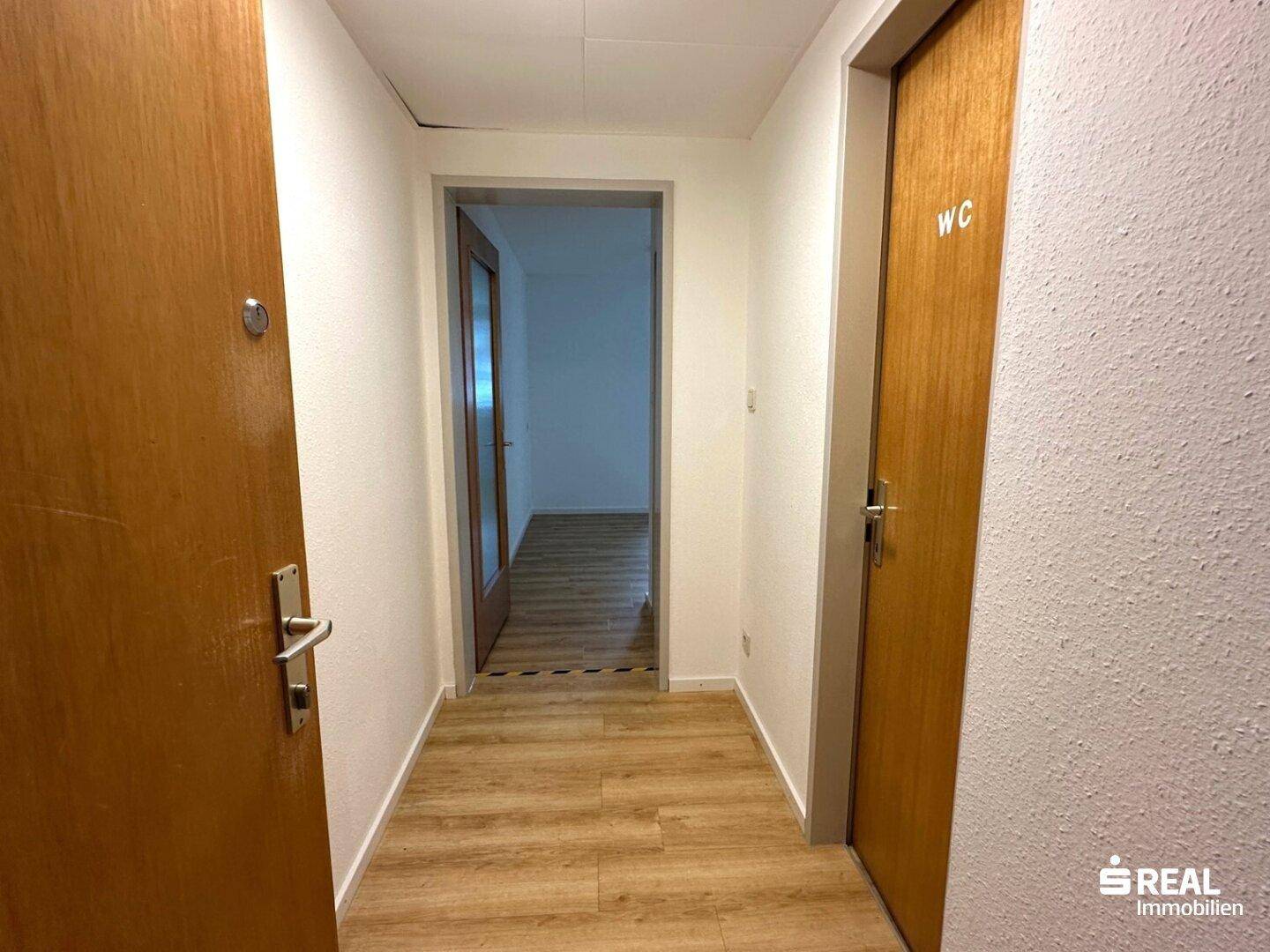 Heller Flur mit Laminatboden und Holztüren, der zu verschiedenen Räumen führt.