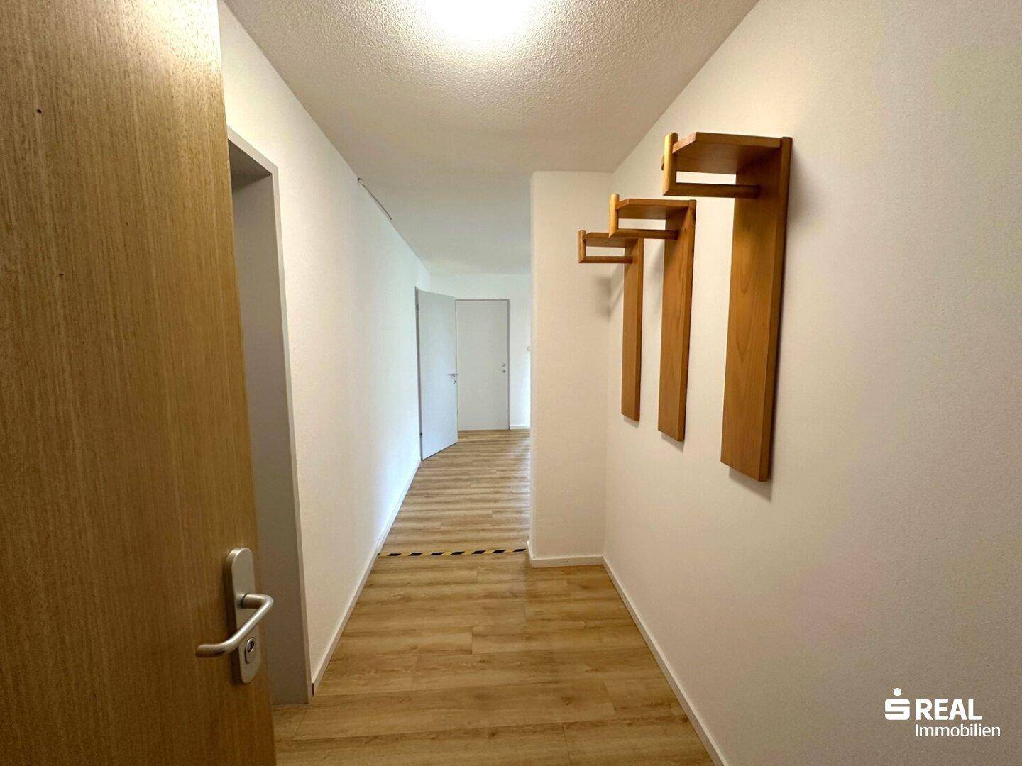 Langer, heller Flur mit Laminatboden und Garderobenhaken, der zu weiteren Räumen führt.
