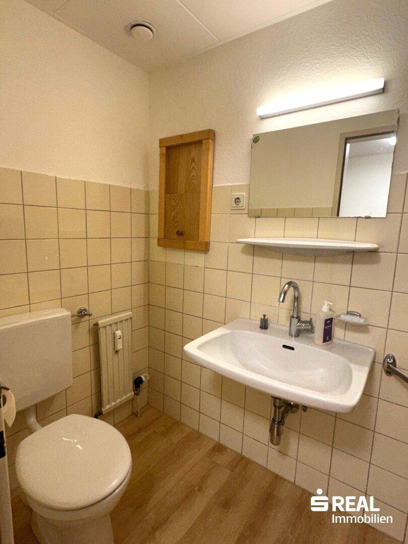 Badezimmer mit WC, Waschbecken und beigefarbenen Fliesen, ausgestattet mit einem Spiegel.
