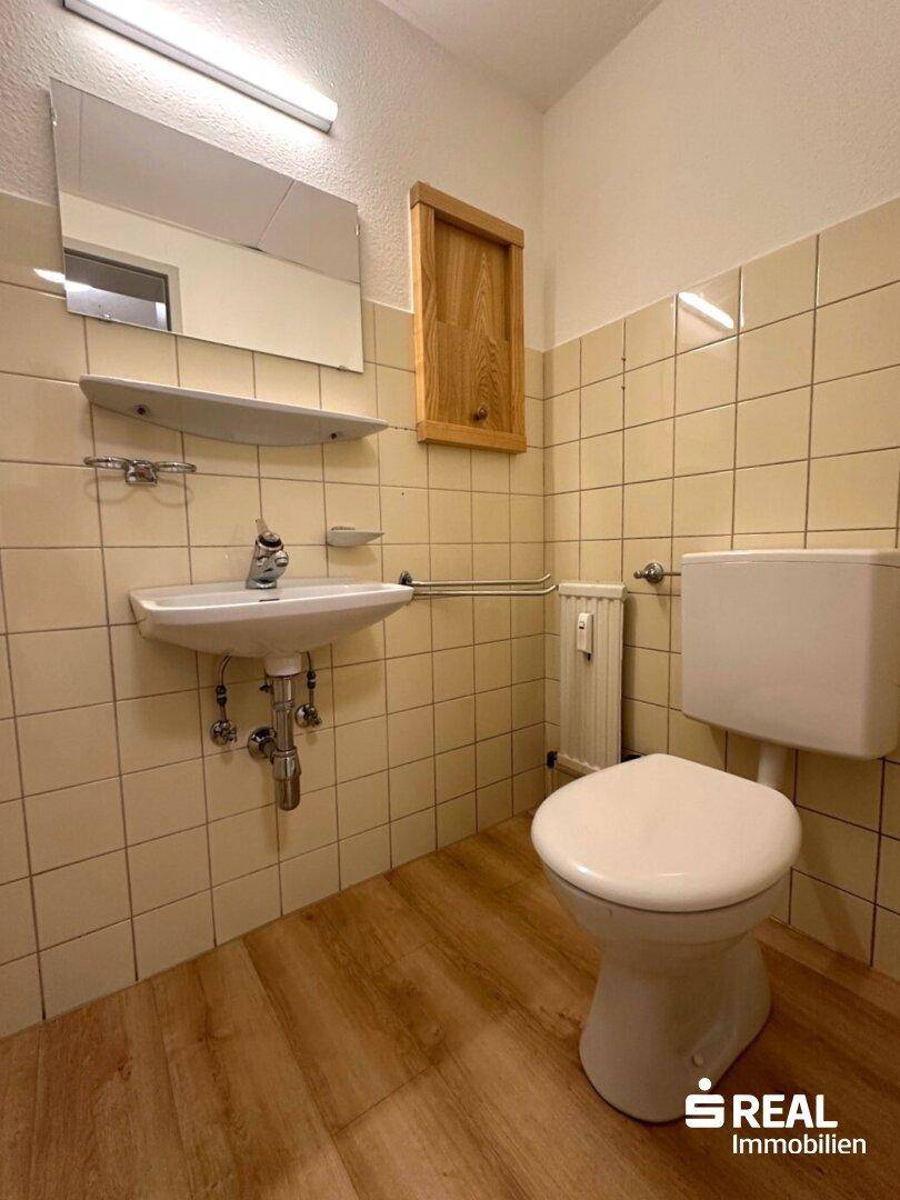 Badezimmer mit WC, Waschbecken und beigefarbenen Fliesen, ausgestattet mit einem Spiegel.