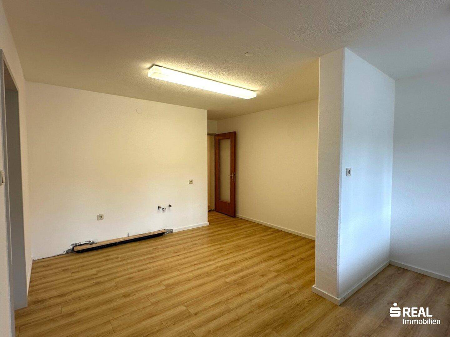 Leerer Raum, vorbereitet für eine Küche, mit Laminatboden und Anschlussmöglichkeiten.