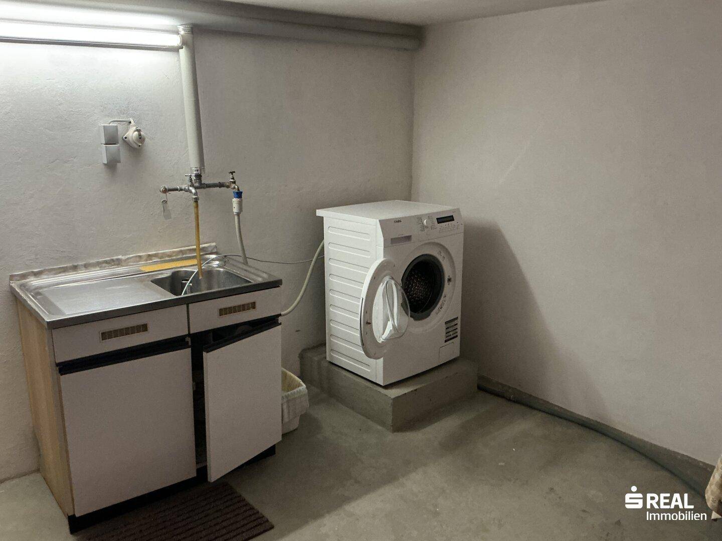 Waschküche im Keller mit Waschmaschine, Spülbecken und viel Stauraum.