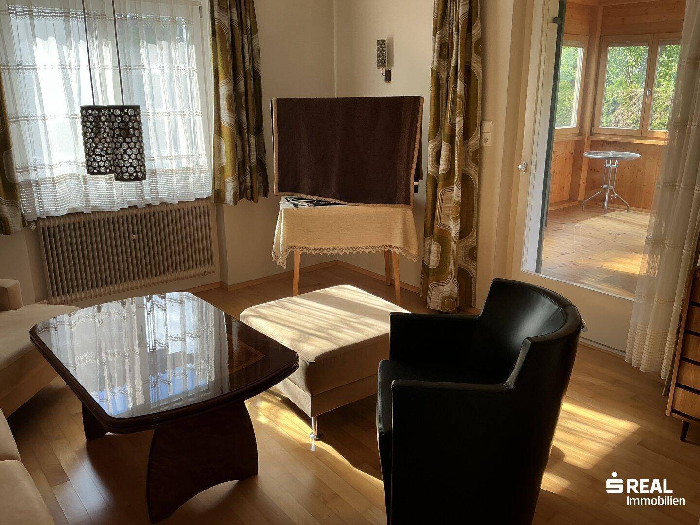 Helles Wohnzimmer mit Parkettboden und Zugang zu einem verglasten Wintergarten.
