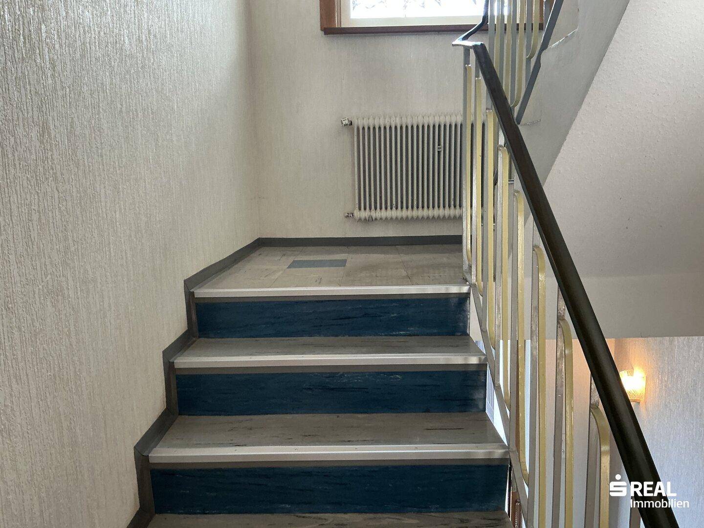 Treppenhaus mit robustem Geländer und strukturierten Tapeten an den Wänden.