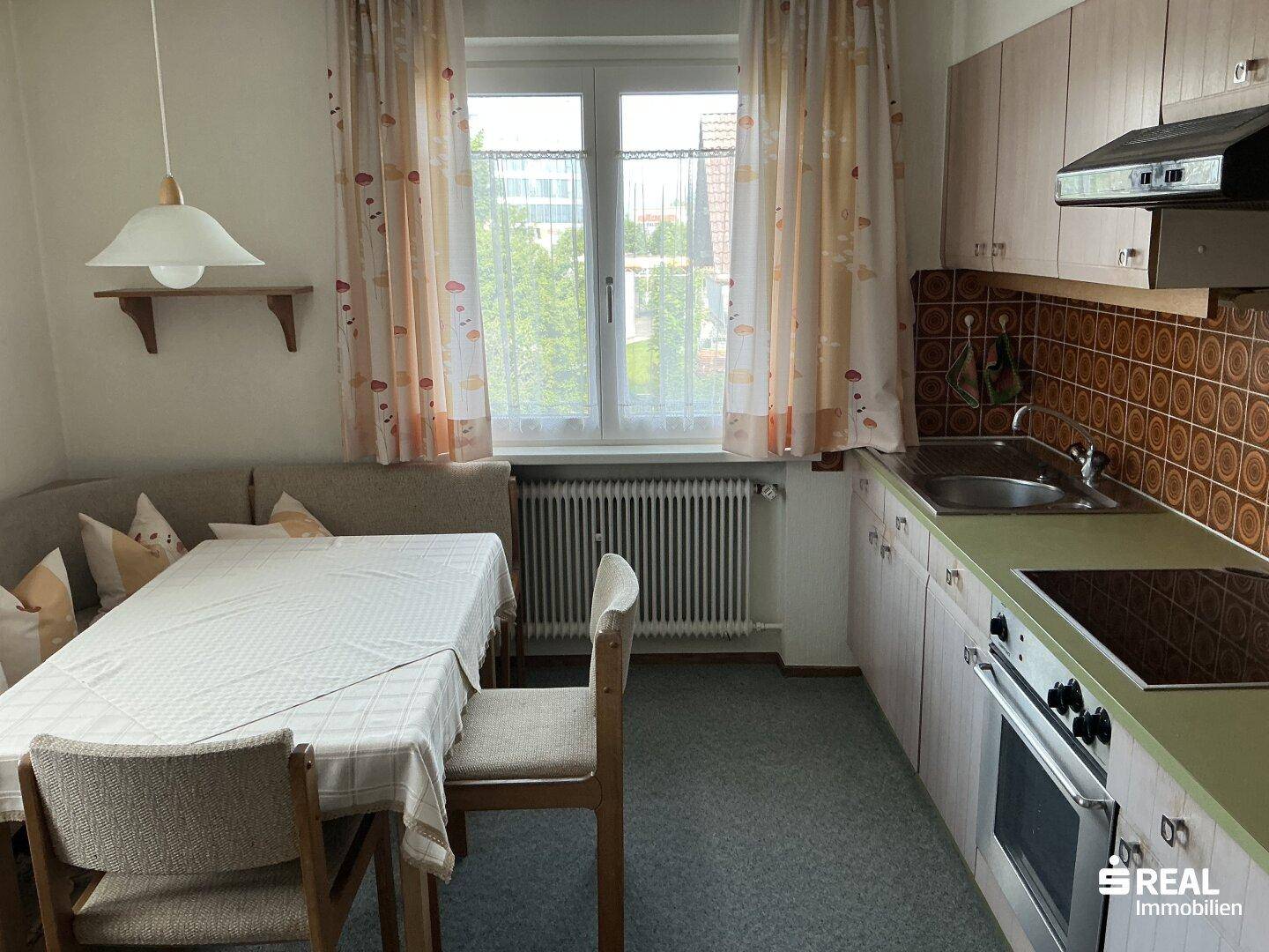 Helle Küche mit Essbereich, hellen Holzschränken und Fenster mit Vorhängen.